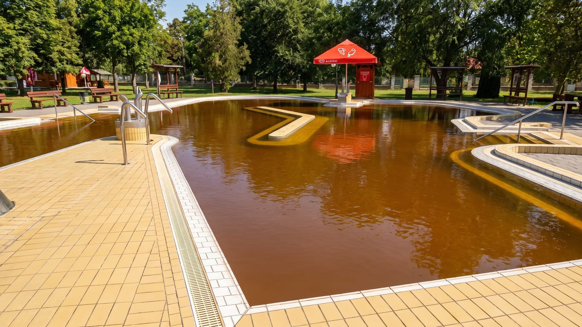 The outdoor thermal pool at Cserkeszolo, its brown mineral water fed by neck-shower jets, with the bath buildings in the park behind.