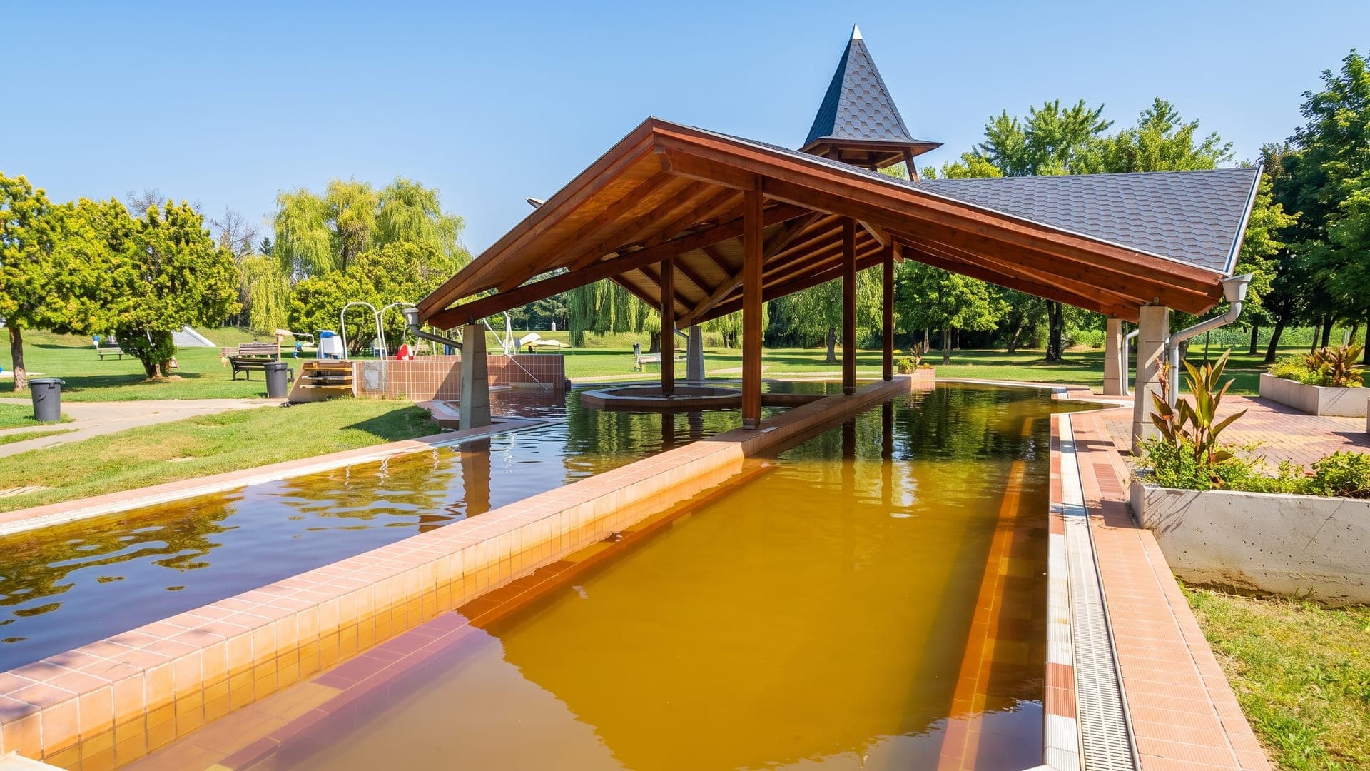 The ochre thermal pool at Csokonyavisonta under its timber pavilion, the yellow water bright against the tiled surround.