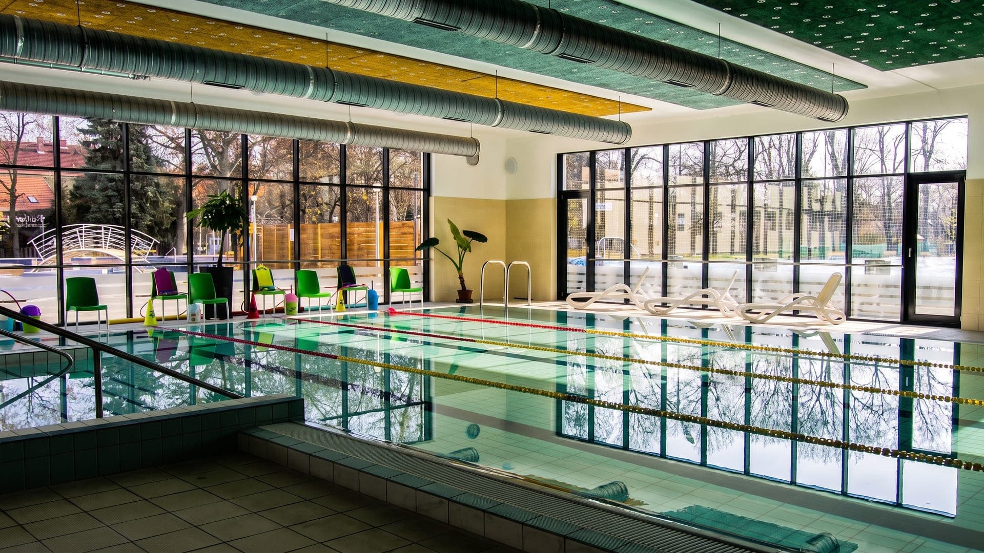 Indoor lane pool in a glass-walled hall with green chairs along the side