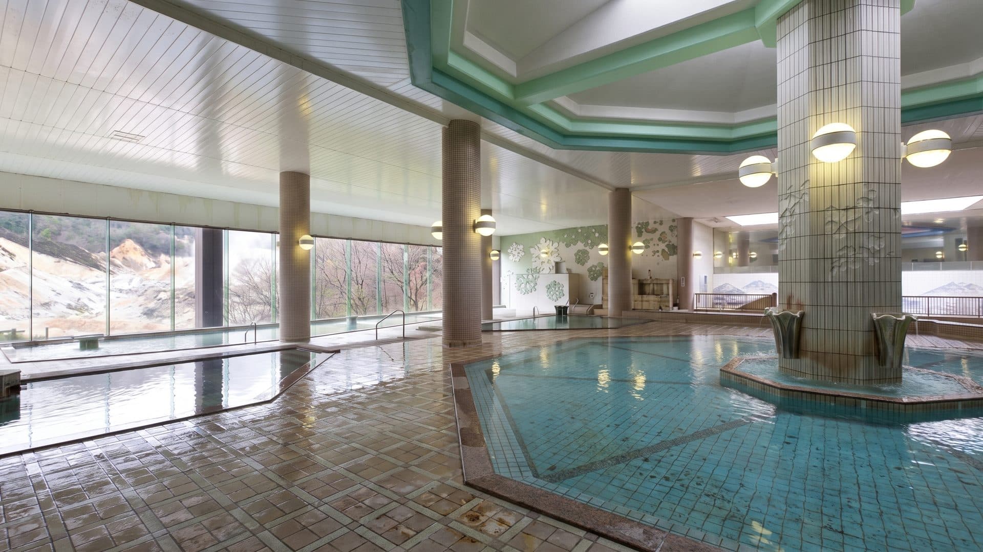 The tiled indoor bathing hall at Dai-ichi Takimotokan in Noboribetsu, with square columns and hanging globe lamps