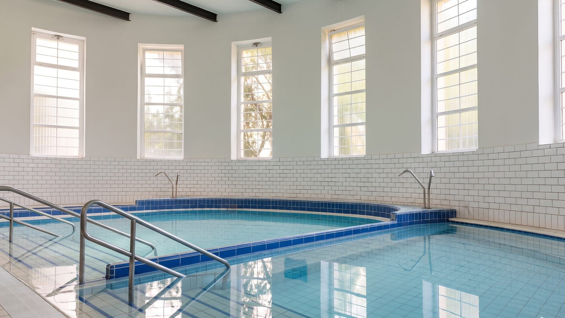 Small tiled indoor pool in a white hall with tall arched windows