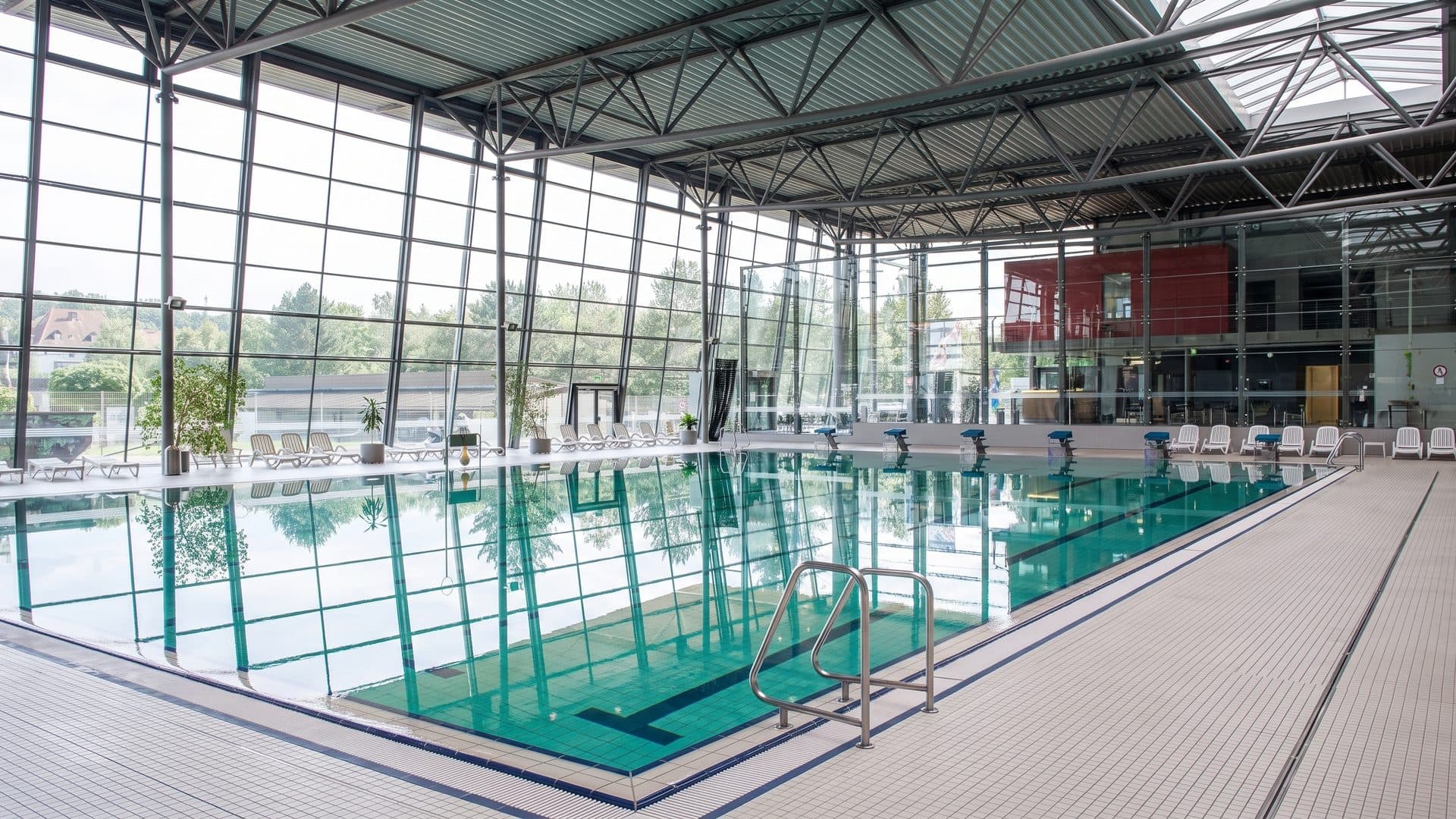 The indoor hall of Das Blau with its glazed wall and steel roof trusses over a green-tiled lane pool