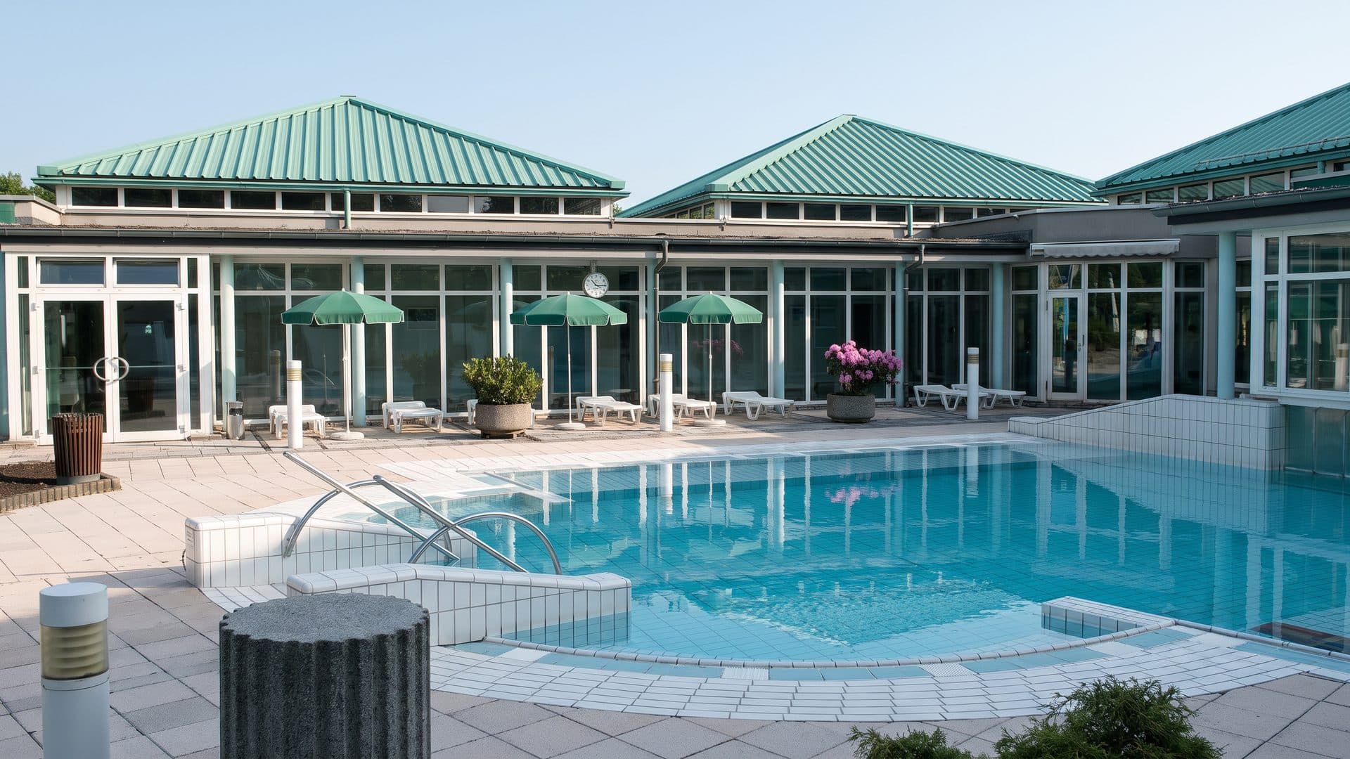 The outdoor pool of the Driburg Therme in front of the glazed spa building with parasols along the deck
