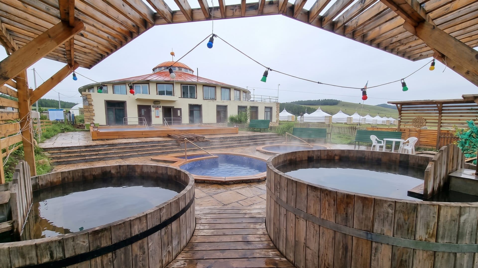 Wooden hot tubs on the timber deck at Duut Resort by the Tsenkher hot springs, with the round lodge behind