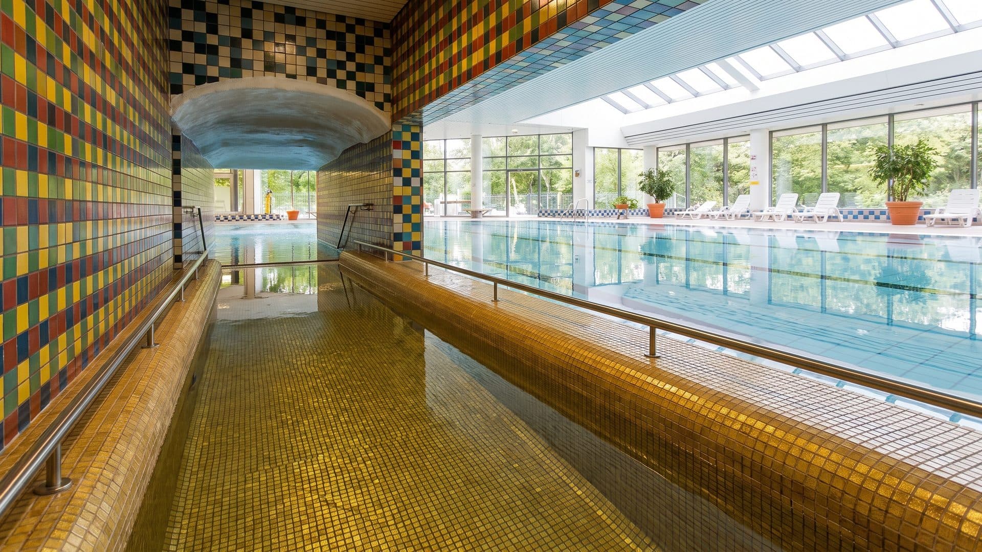 The gold-mosaic channel of Eriksdalsbadet running through the pool hall