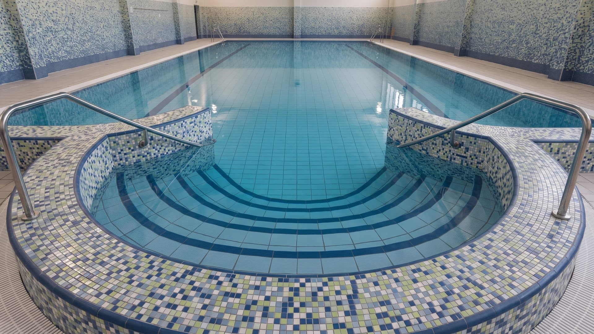 The indoor pool of Erlebnisbad Aquafit in Waldmuenchen with its mosaic-tiled surround and handrails