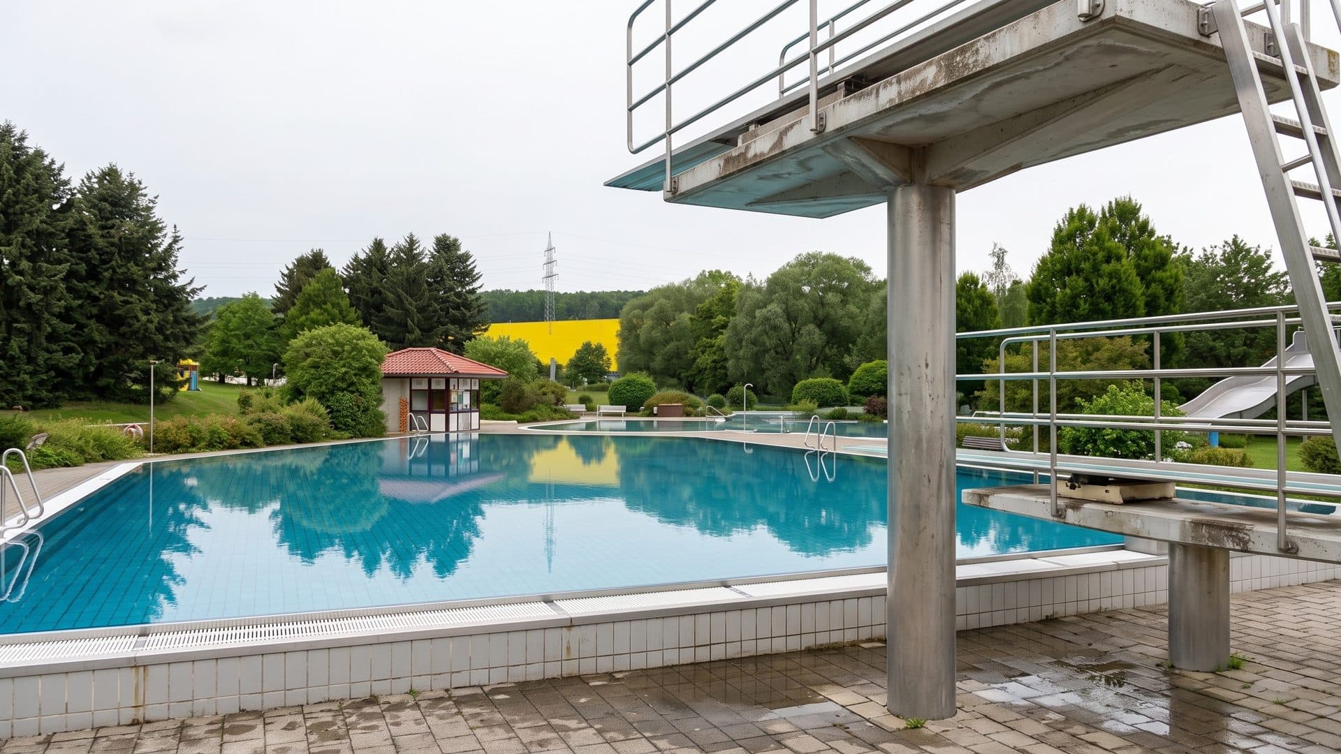 The outdoor pool of the Erlebnisbad Oederan with a diving platform, a small pavilion and trees
