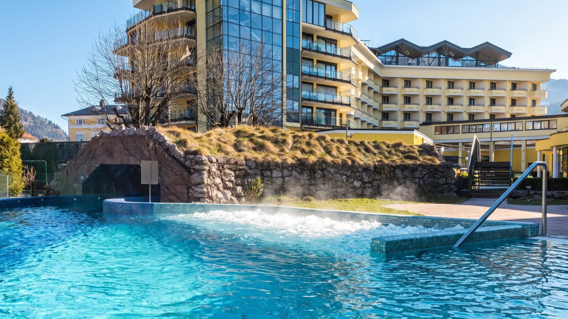 Outdoor pool with bubbling water below the hotel terraces, a rock wall and steam rising