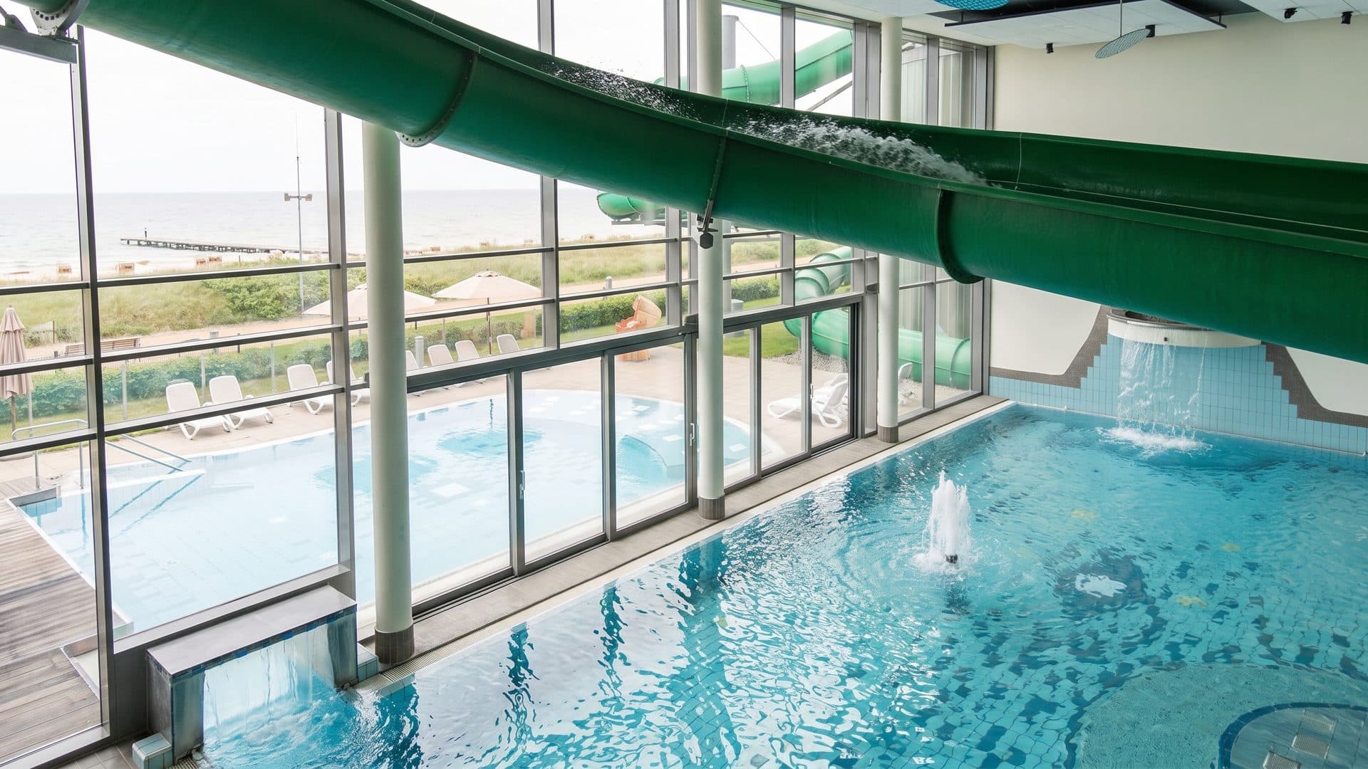 The indoor pool at FehMare with the green flume crossing above the water and the Baltic beyond the glass