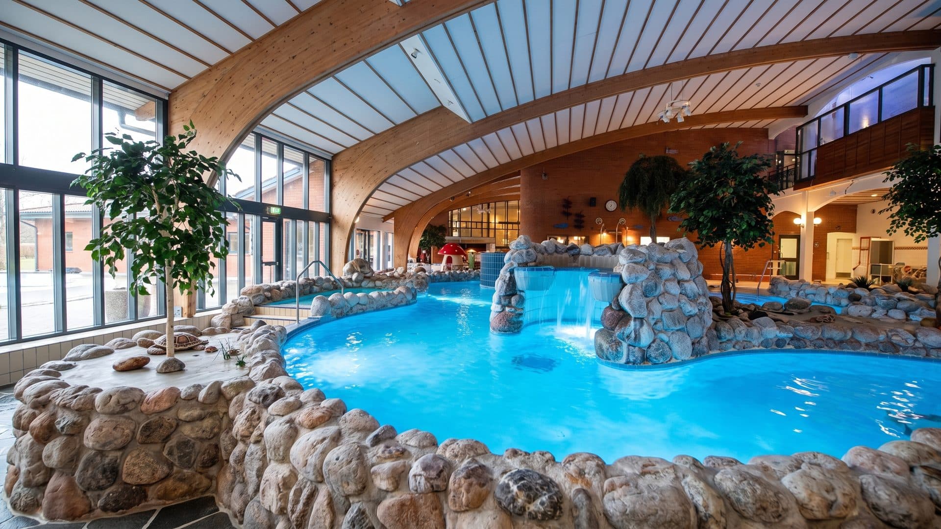 The adventure pool of the Fjärran Höjder baths around its rock outcrop under the curved timber roof