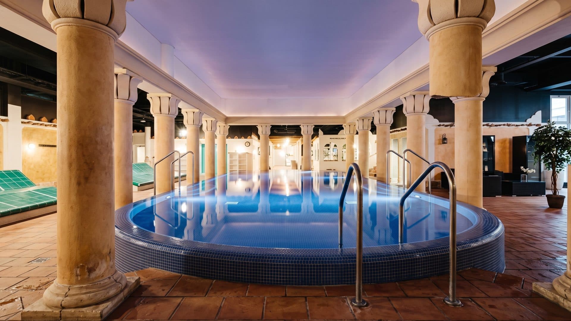 The oval indoor pool of Flamingo Spa in Vantaa between tall columns under a softly lit ceiling