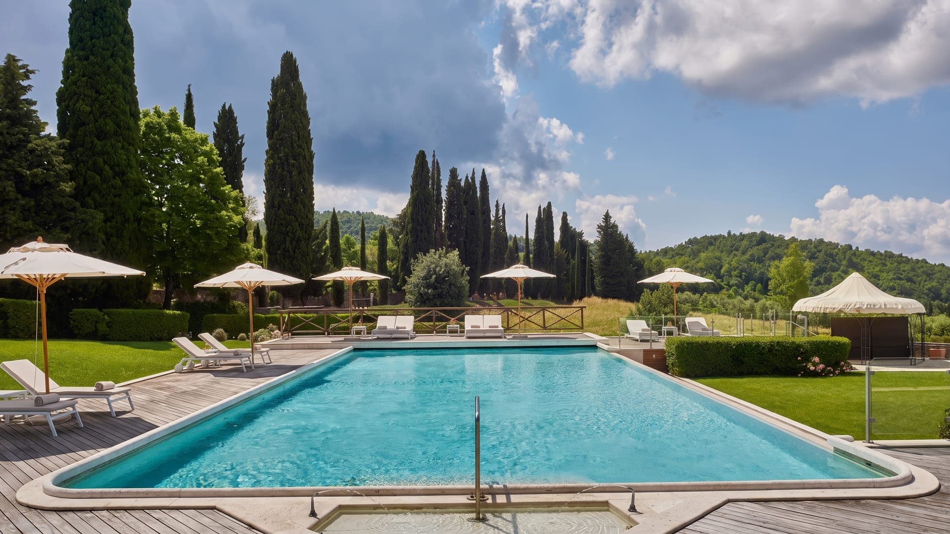 Outdoor pool with cypresses and parasols above the Tuscan hills