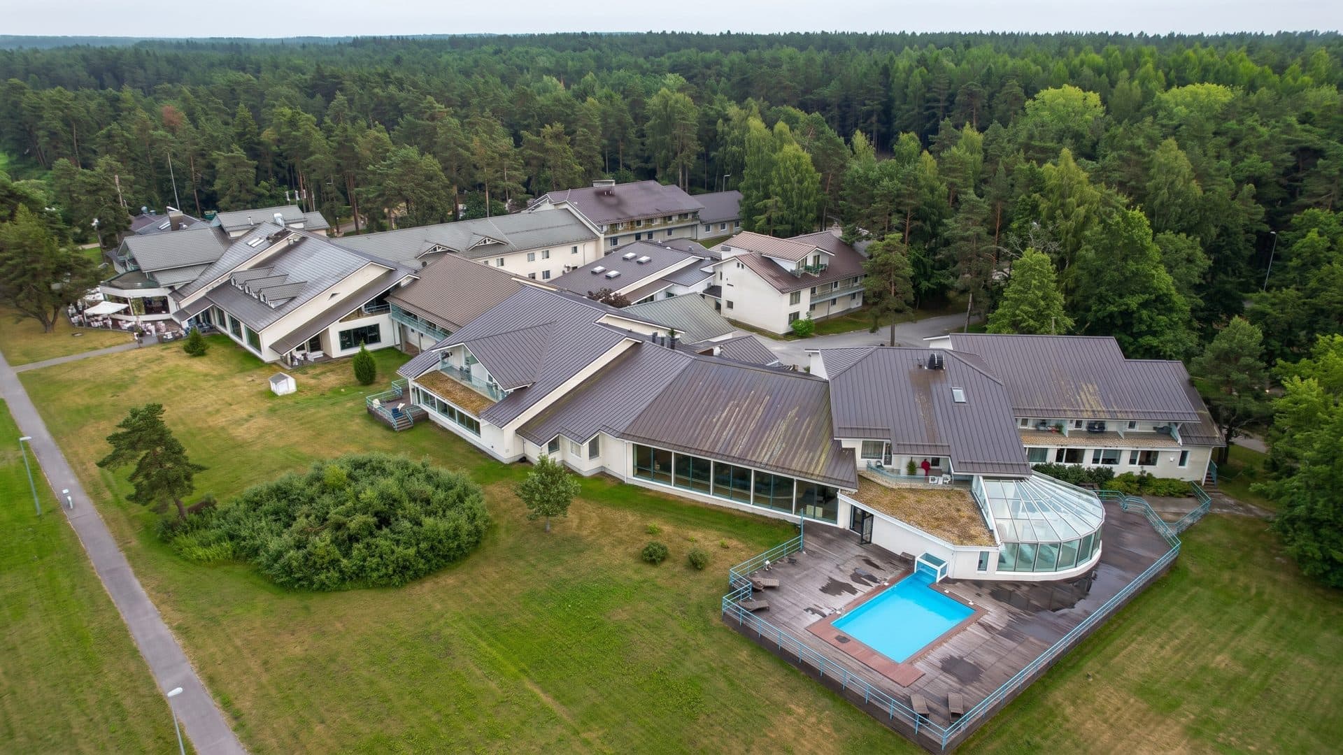 Fra Mare in Haapsalu from the air: low white buildings with dark hipped roofs and the outdoor pool, ringed by pine forest