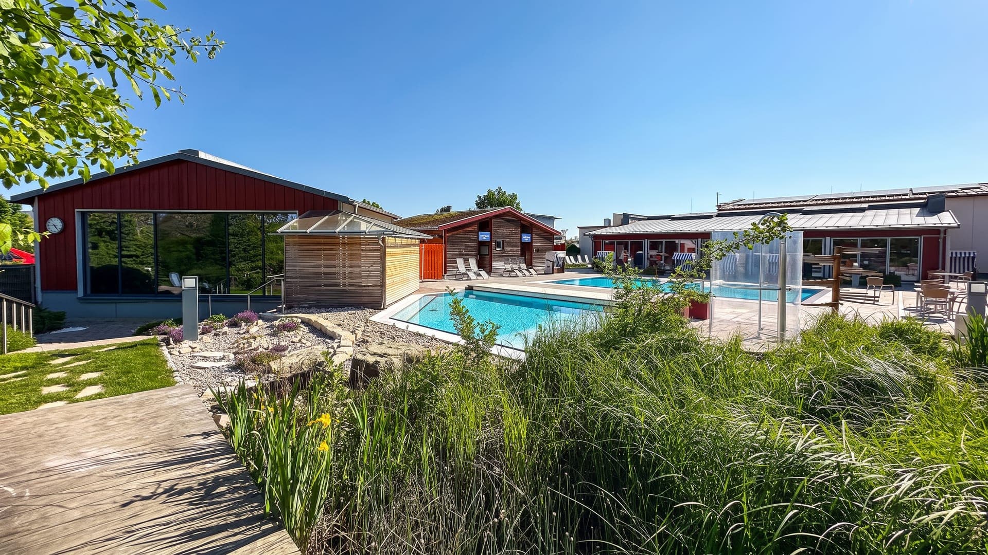 An outdoor thermal pool at Franken-Therme in Bad Windsheim, beside the red timber bathing houses, with reeds and a boardwalk in the foreground.