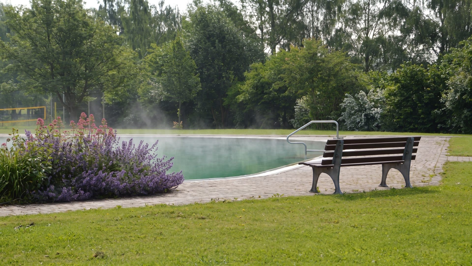 The steaming outdoor thermal pool at the Frankentherme, with a bench and a wicker beach chair on the lawn