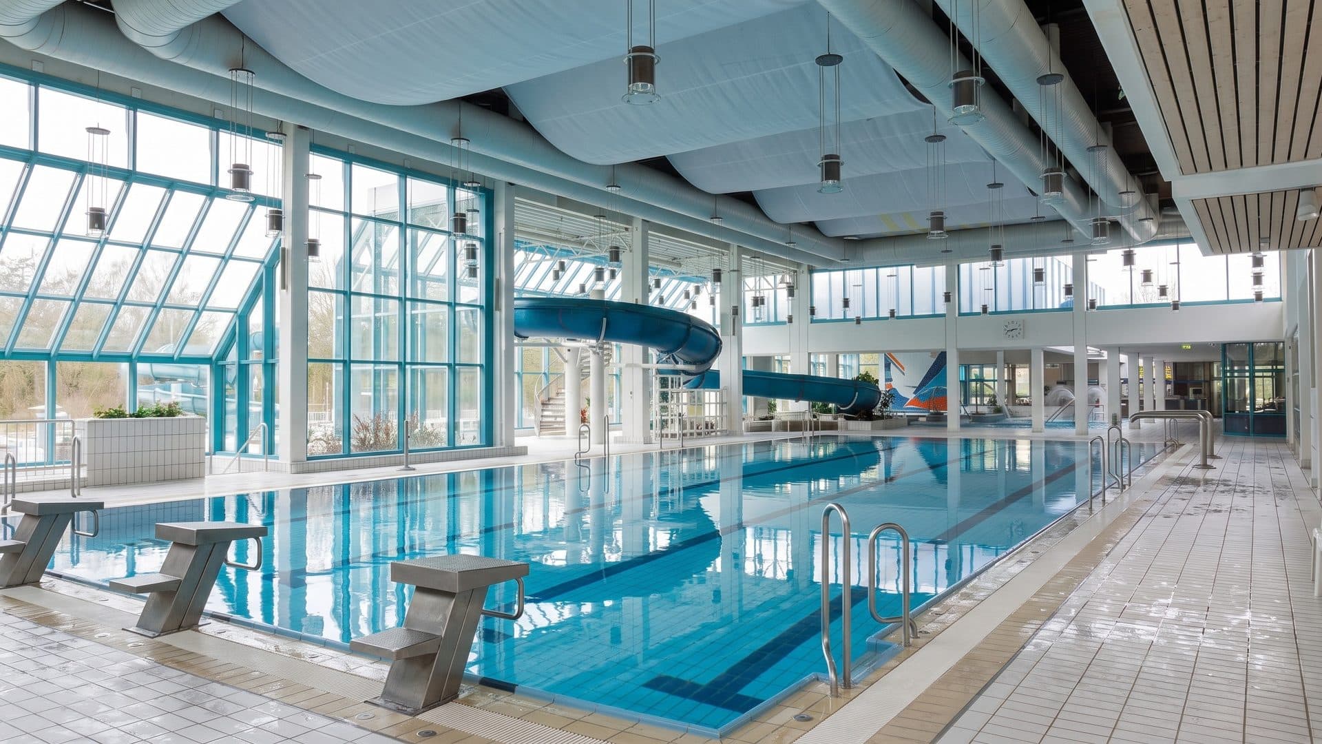 Indoor sports pool with starting blocks, a glazed wall and a blue tube slide at the far end