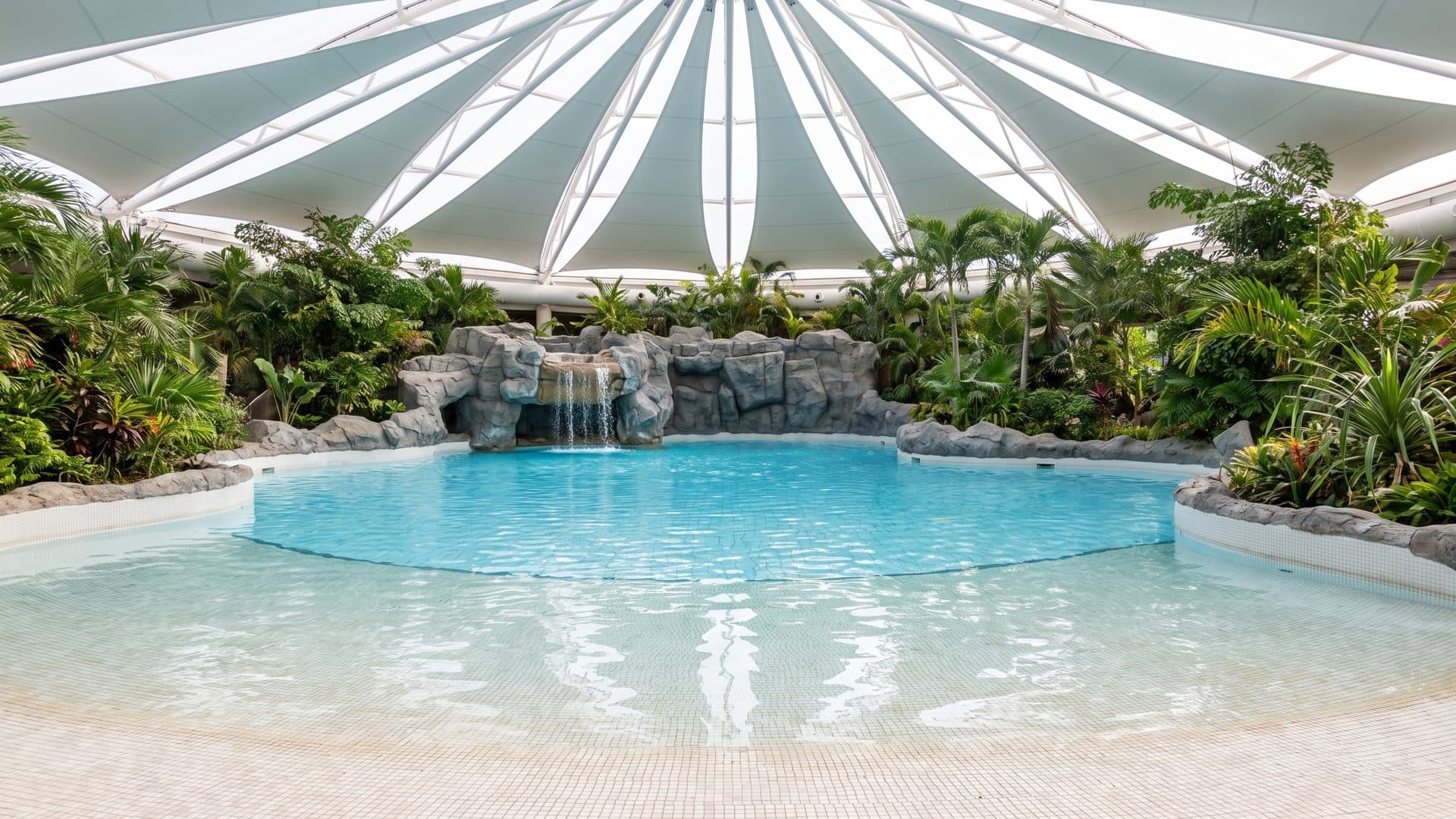 The lagoon pool of the Greifensteine leisure baths with its rock waterfall under the white tensile roof