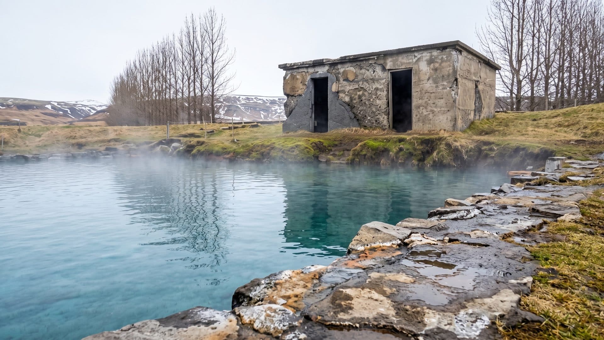 The steaming natural hot pool of Gamla Laugin in Fludir with the old stone changing hut and bare trees