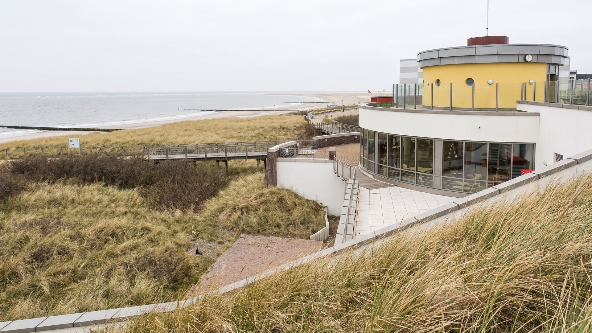 The curved coastal building of the Gezeitenland baths among the dunes above the sea