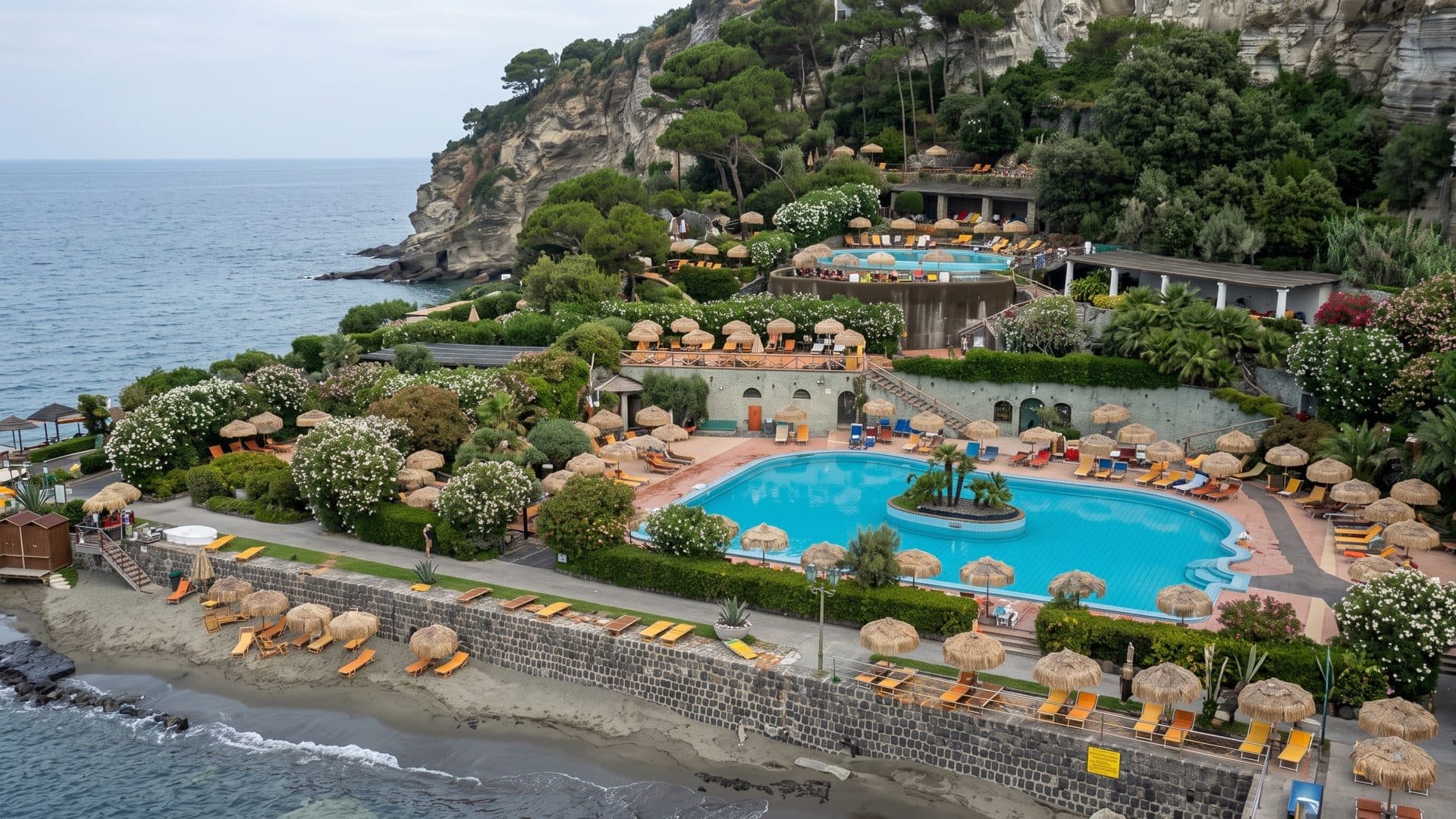 Aerial view of the Giardini Poseidon thermal gardens on Ischia: pools among parasols and greenery above the sea