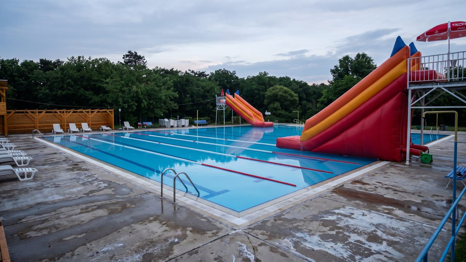 Outdoor lap pool with lane ropes and a large red and yellow inflatable-style slide tower