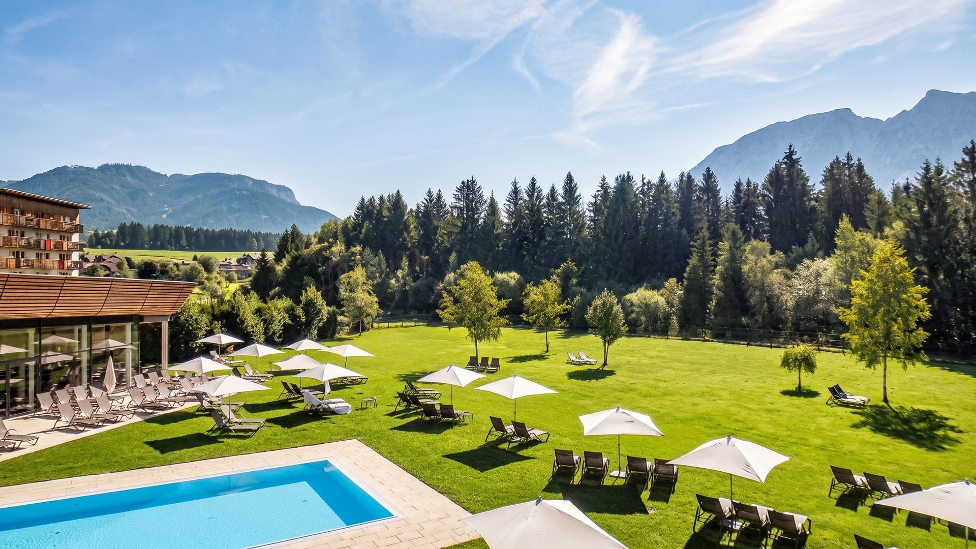 Lawn with parasols and loungers beside the outdoor pool, mountains rising behind