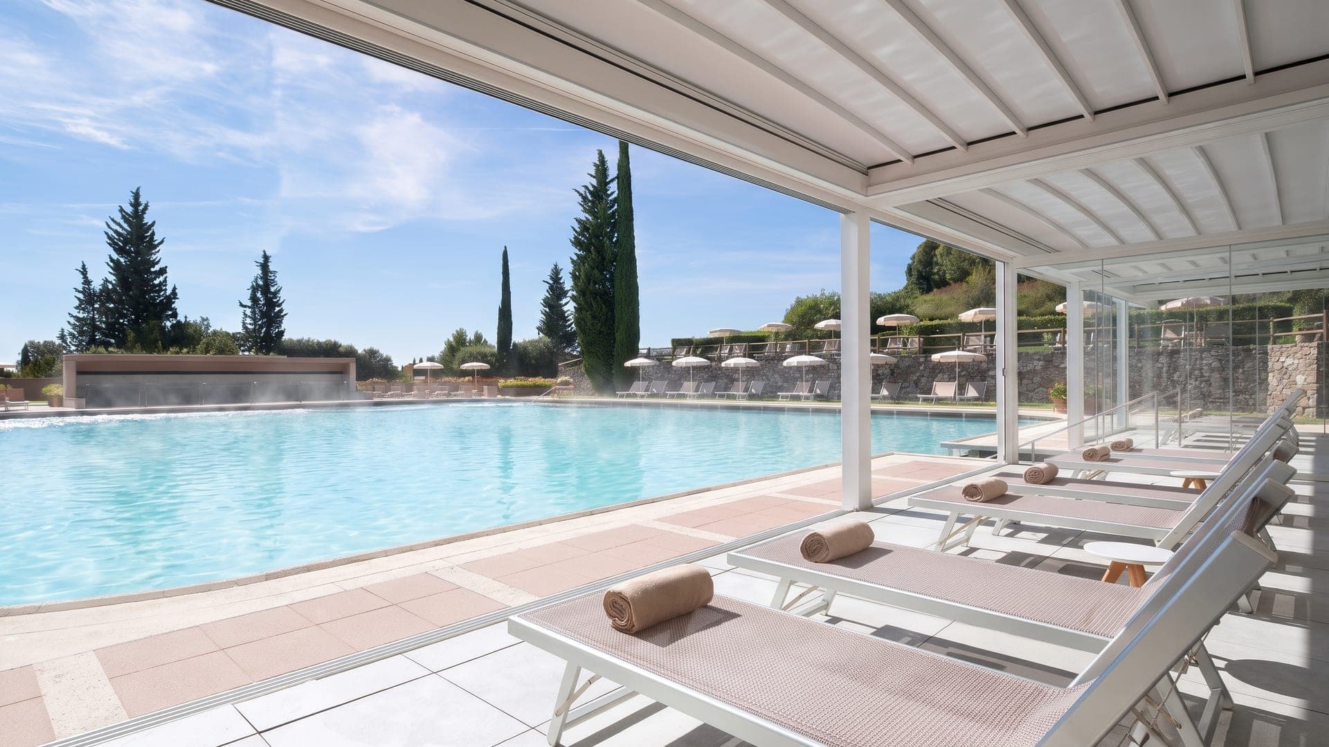 Steaming outdoor pool under a white canopy, cypresses beyond