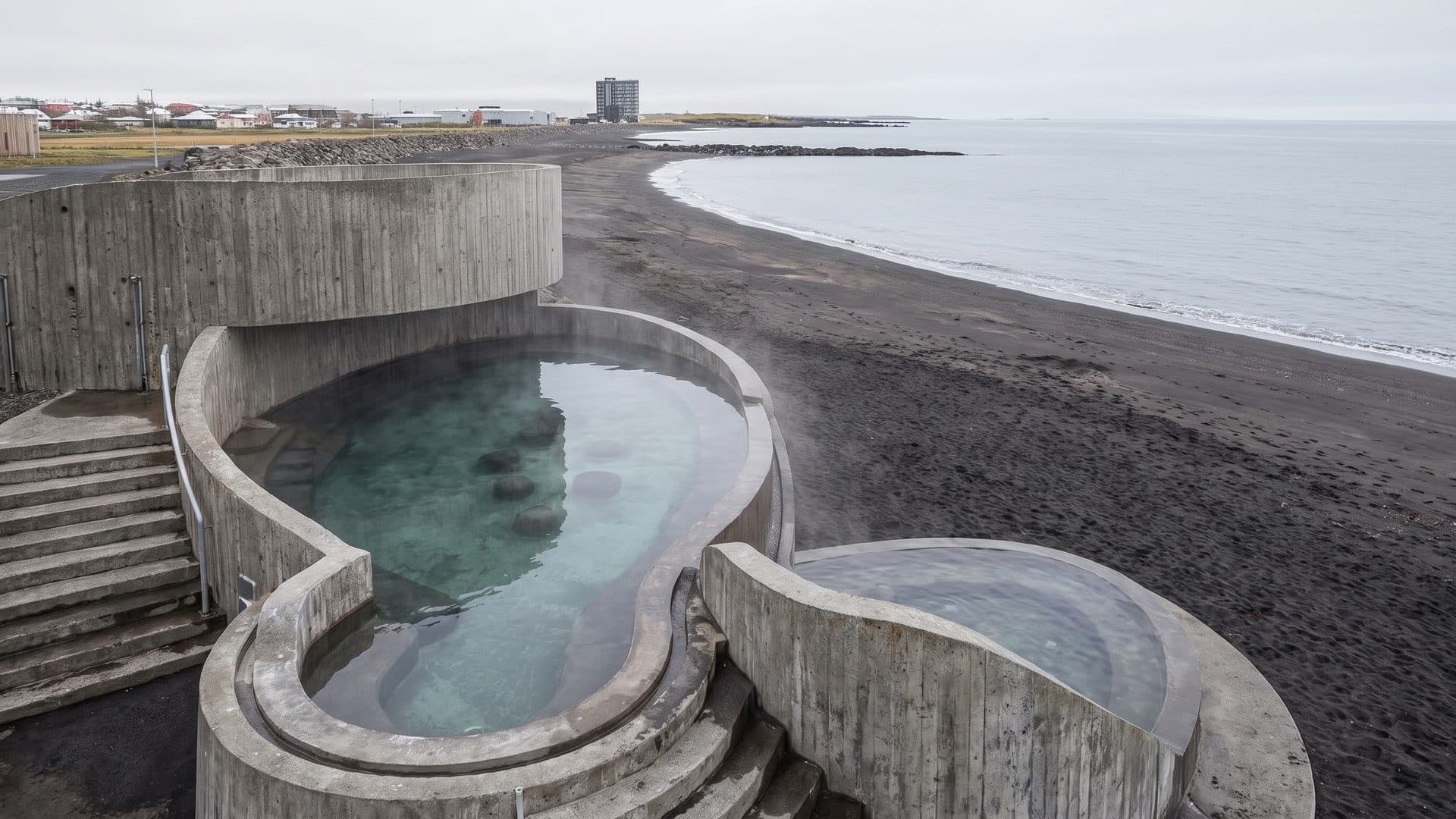 The concrete Gudlaug hot pool on the black basalt shore with the sea behind