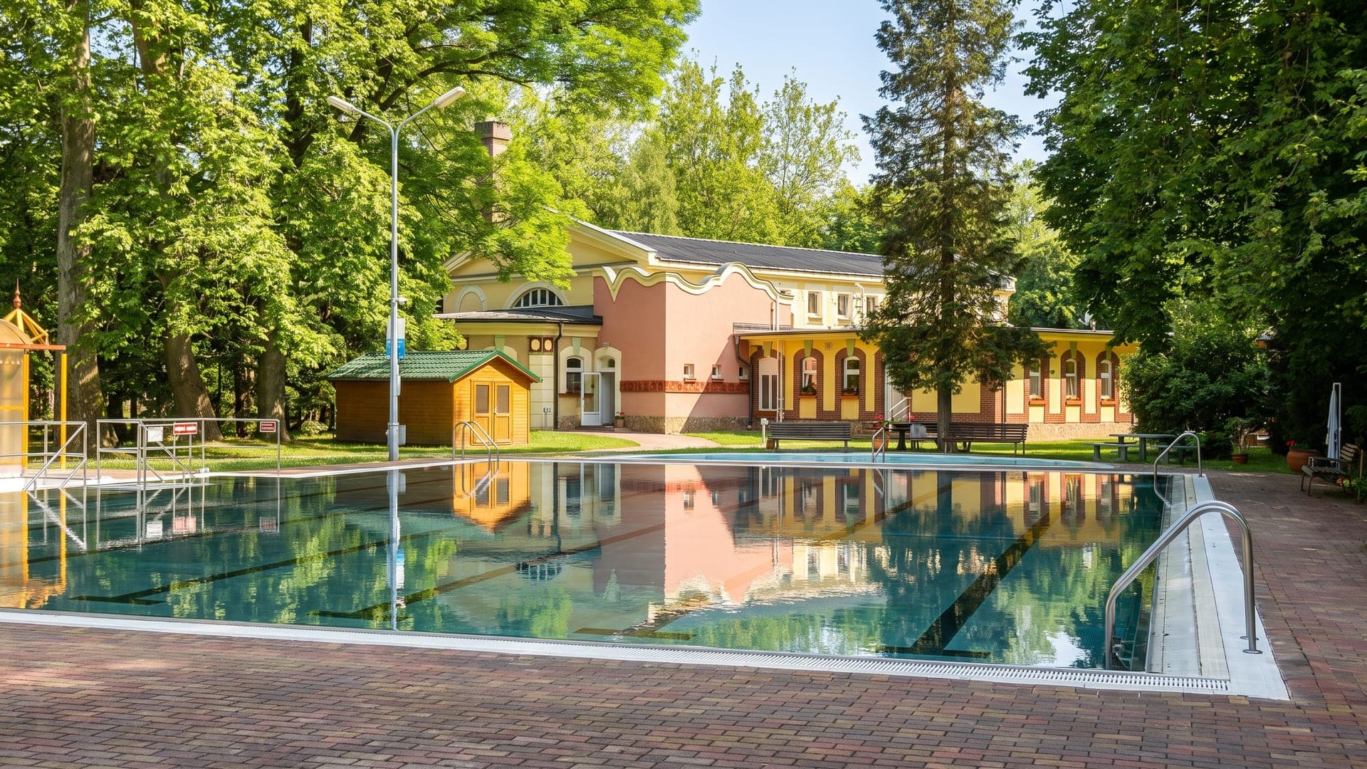 Outdoor pool in front of a pale historic bath building among mature trees
