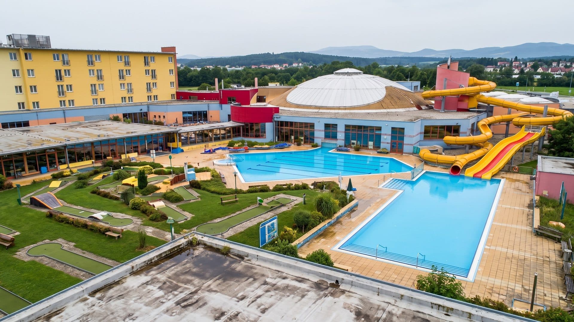 The resort seen from above, its outdoor pools and yellow slides between the hotel, the white dome and a mini-golf course