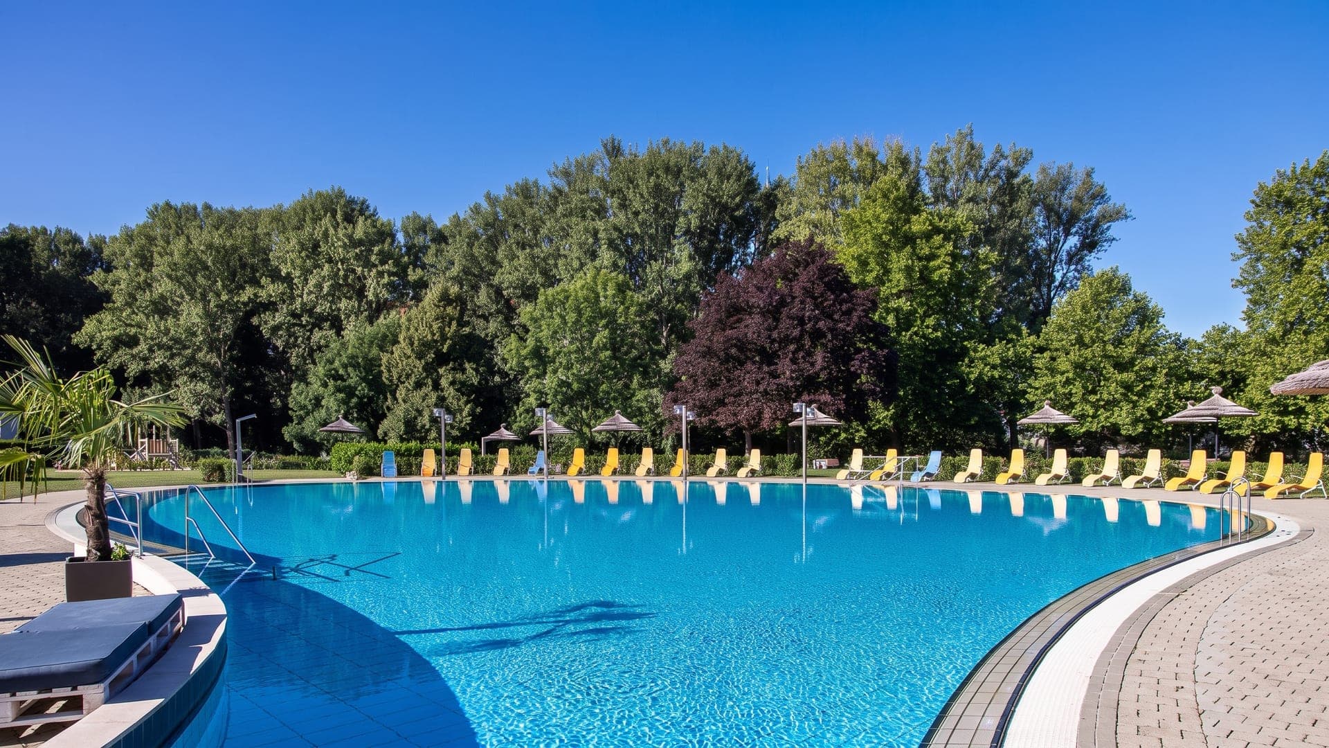 The round outdoor pool at Happyland in Klosterneuburg, ringed by loungers and mature trees.