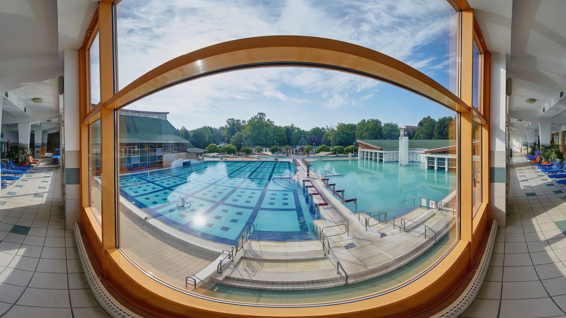 The outdoor pool at the Harkany thermal bath, seen through a tall arched window from inside the bath house.