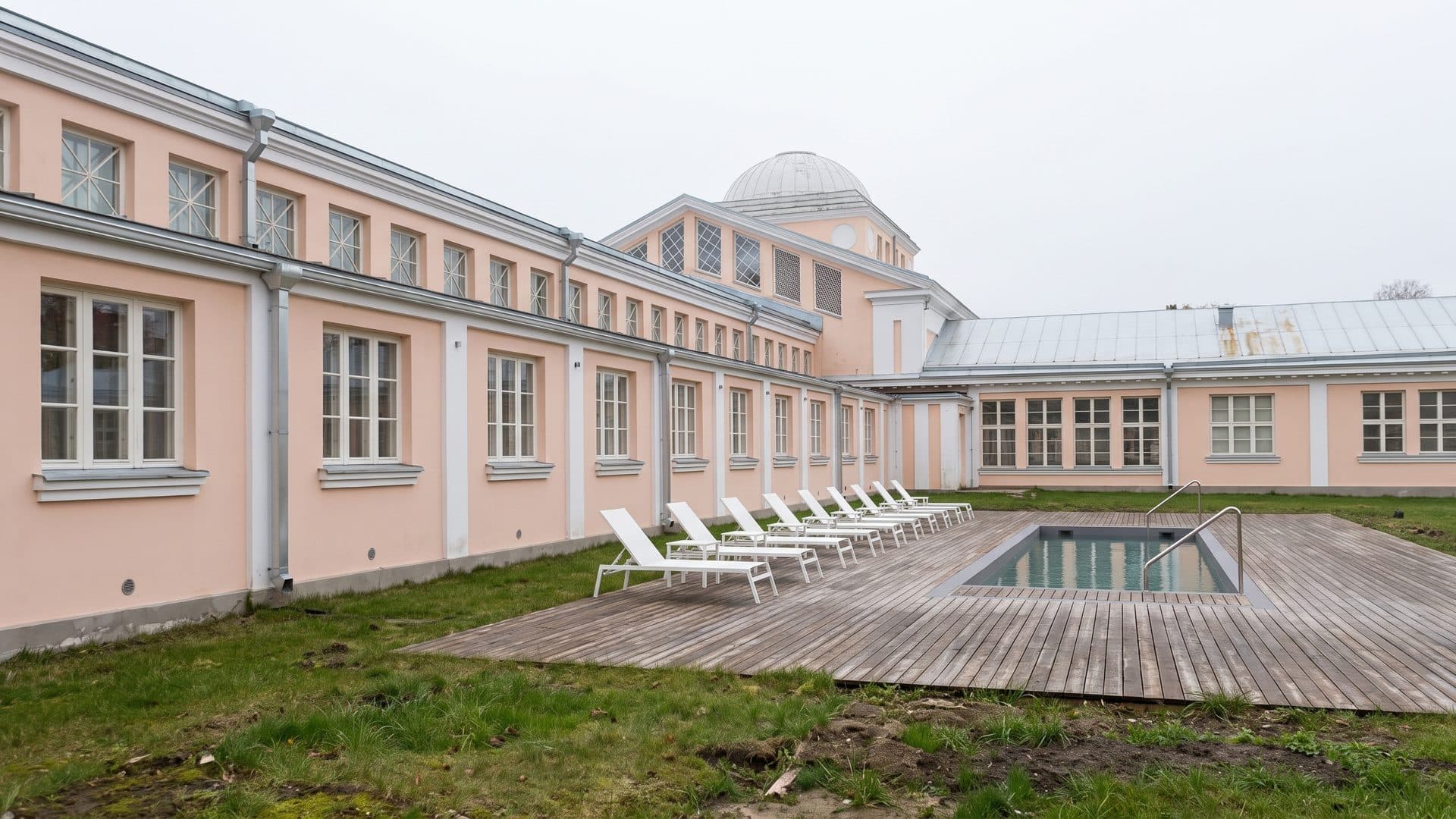 The historic pale bath building of Hedon Spa in Parnu seen along its front, with the outdoor pool and loungers on the deck