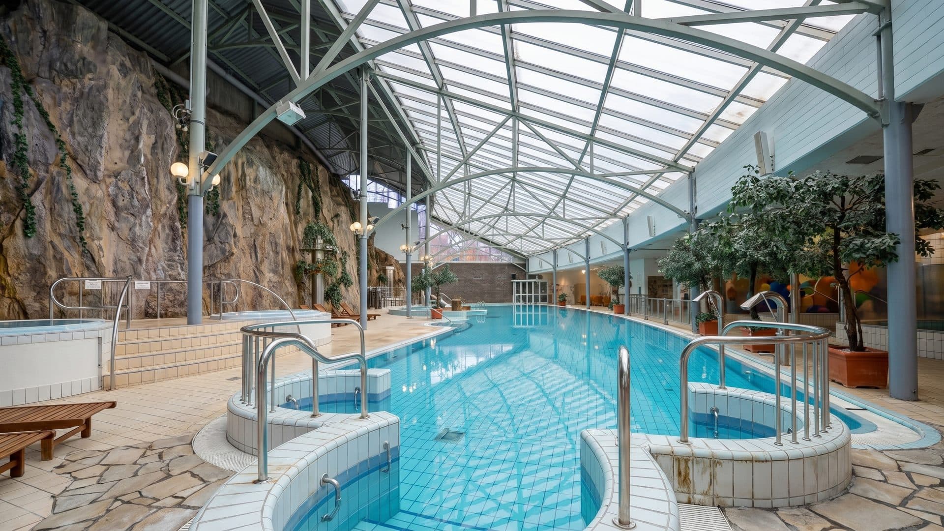 The pool hall at Holiday Club Tampereen Kehraamo under its glazed barrel vault, the rock face along one side and whirlpool basins set into the water