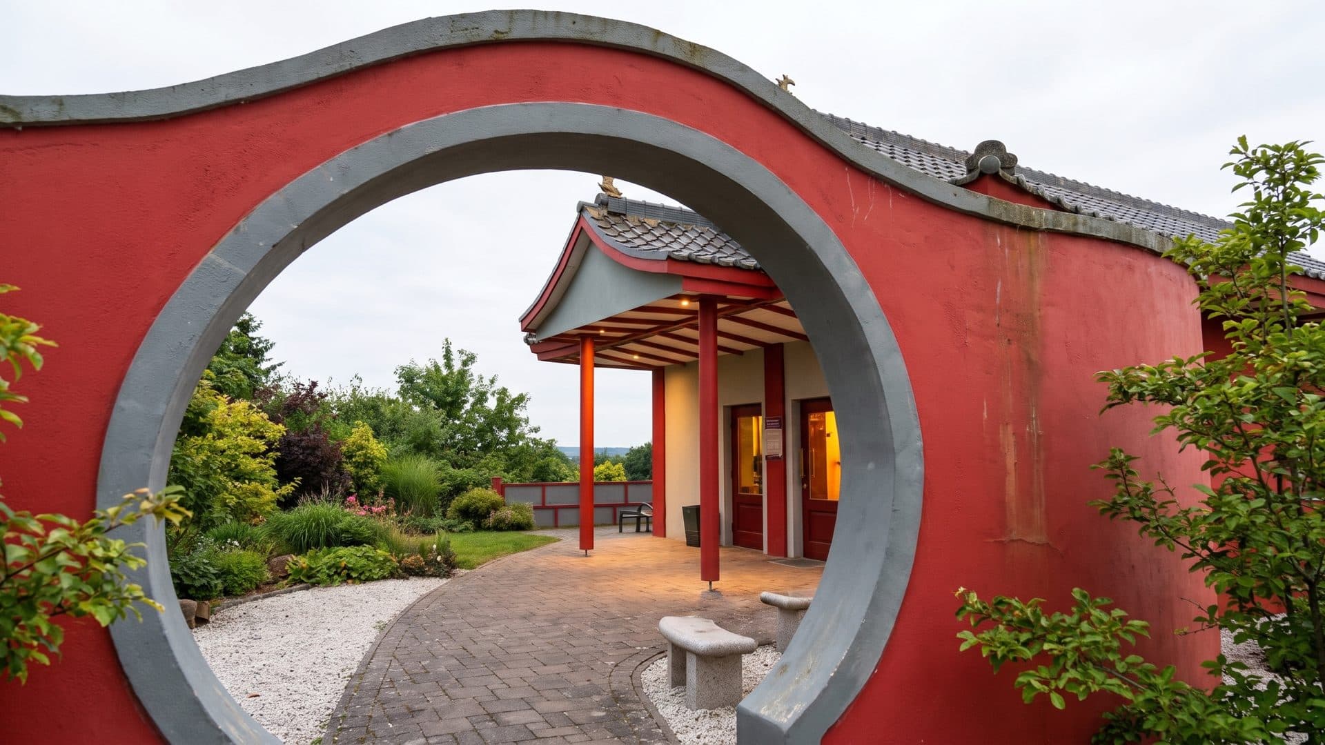 The round arch in the red garden wall at the HolstenTherme, with the timber pavilion standing inside it