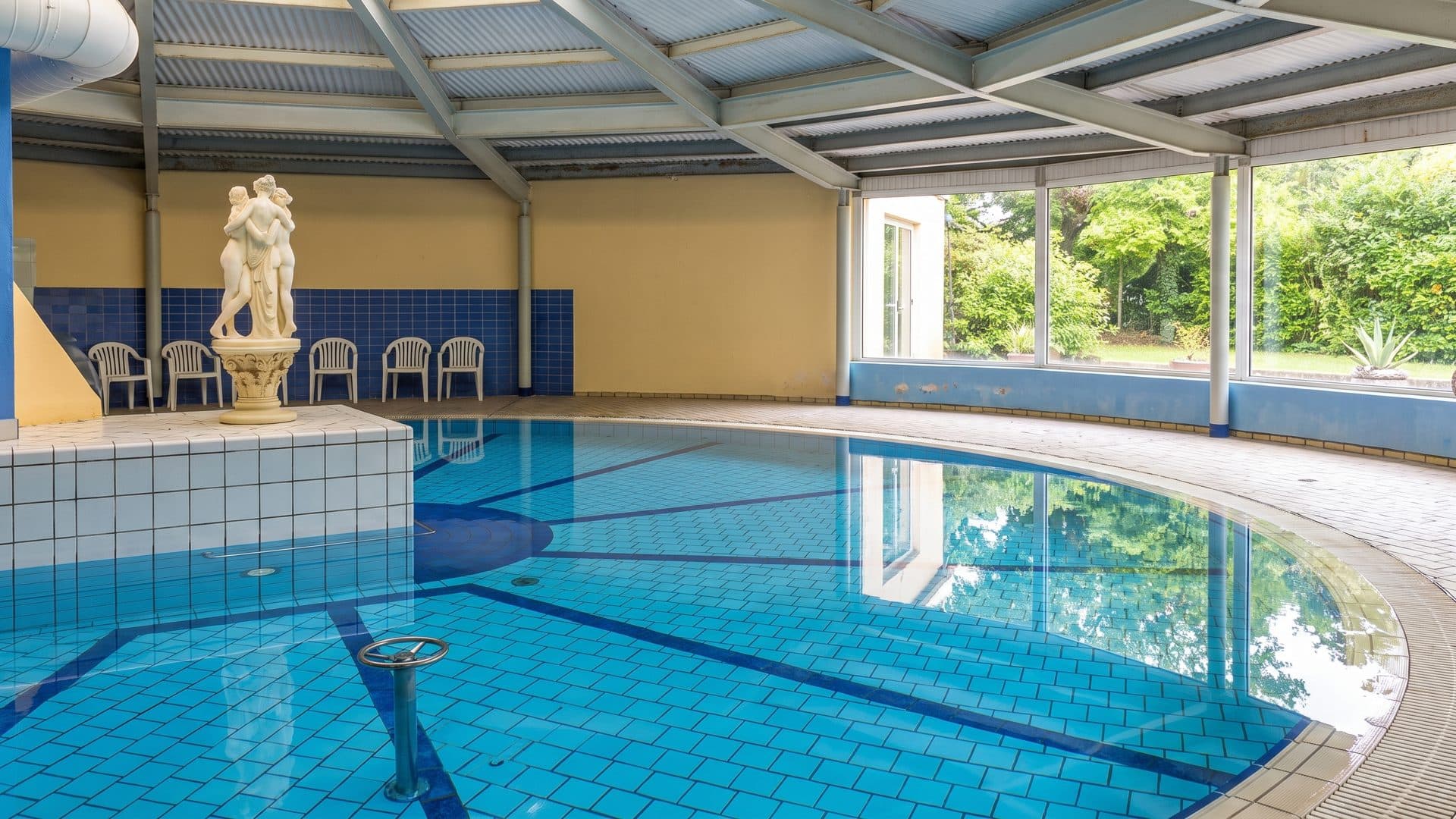 The indoor spa pool at Hotel Balneari de Vallfogona de Riucorb, with a classical statue beside the water.