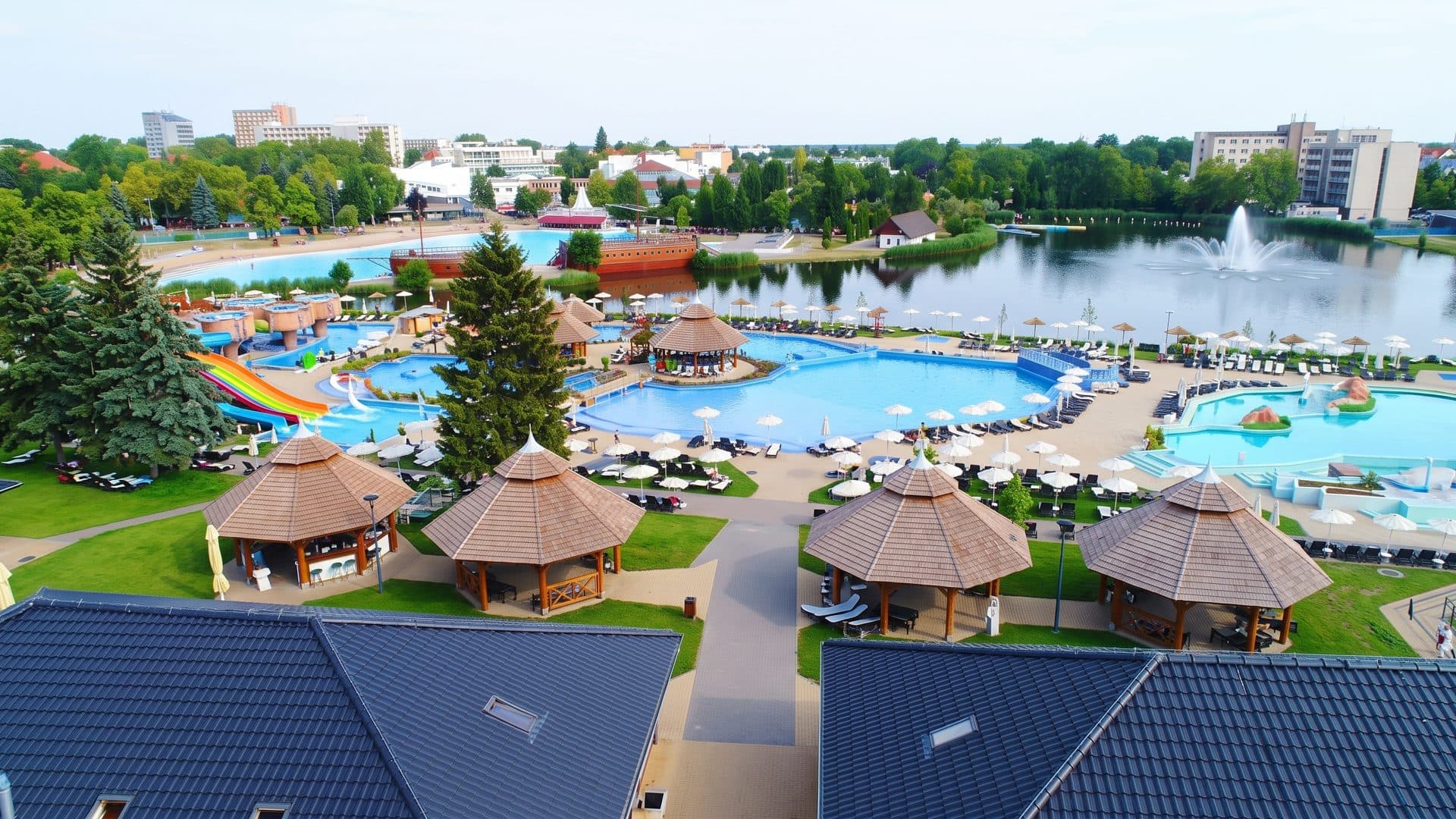 The spa park from above: thatched pavilions, a chain of pools and the lake with its fountain behind.
