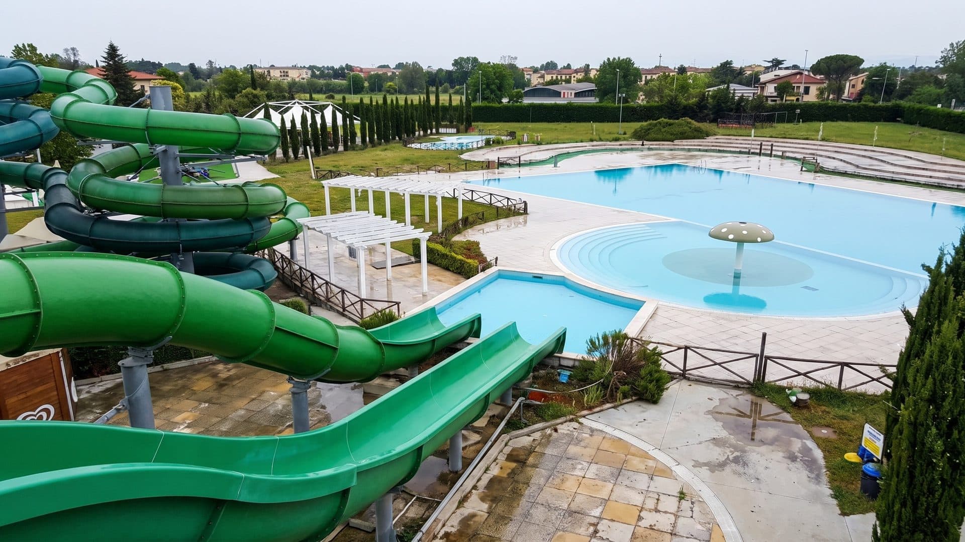 Green spiral waterslides beside the outdoor pools, with a pergola and a mushroom fountain in the leisure pool