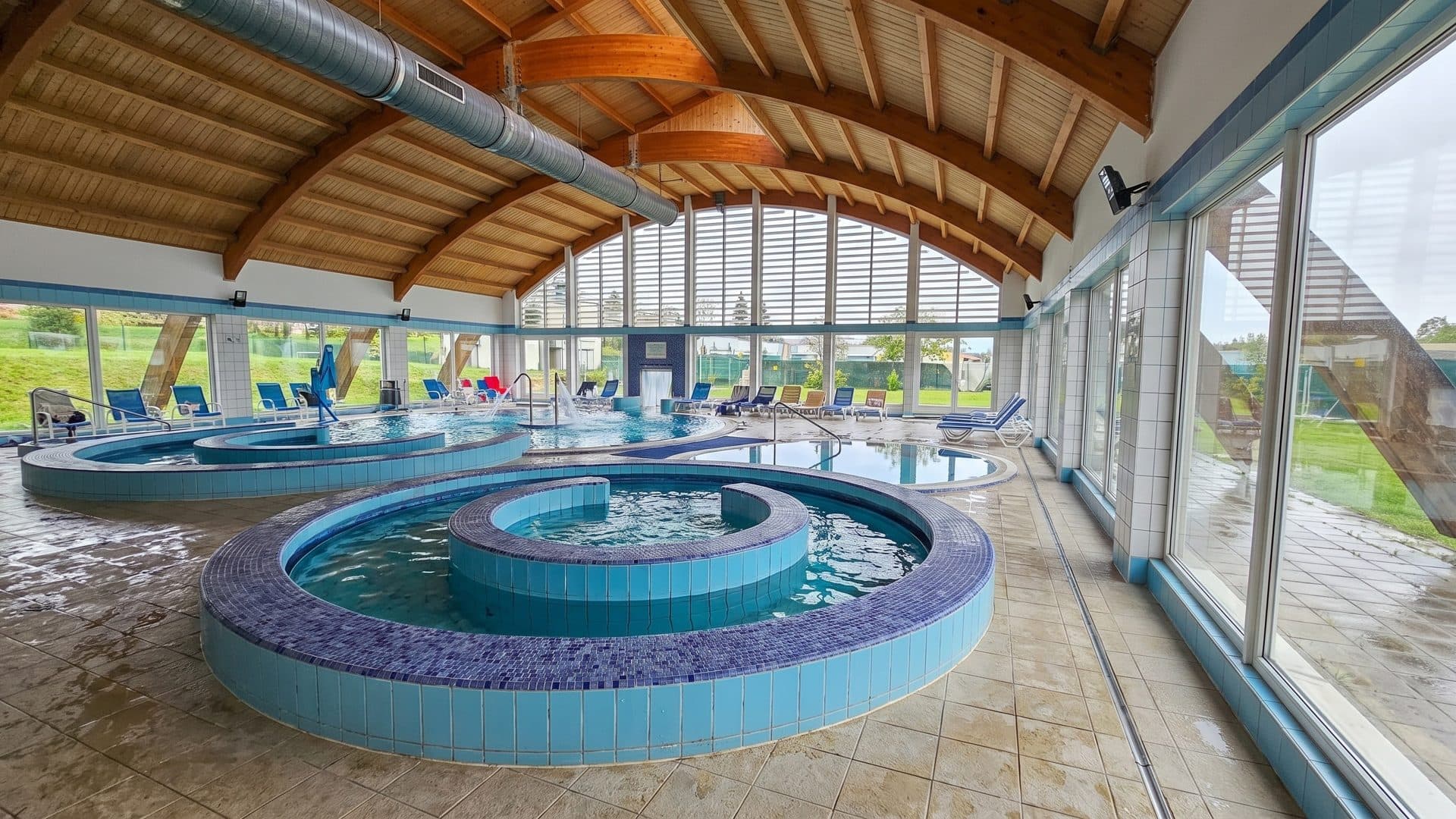Round tiled thermal pools under the arched timber roof of the glazed indoor hall