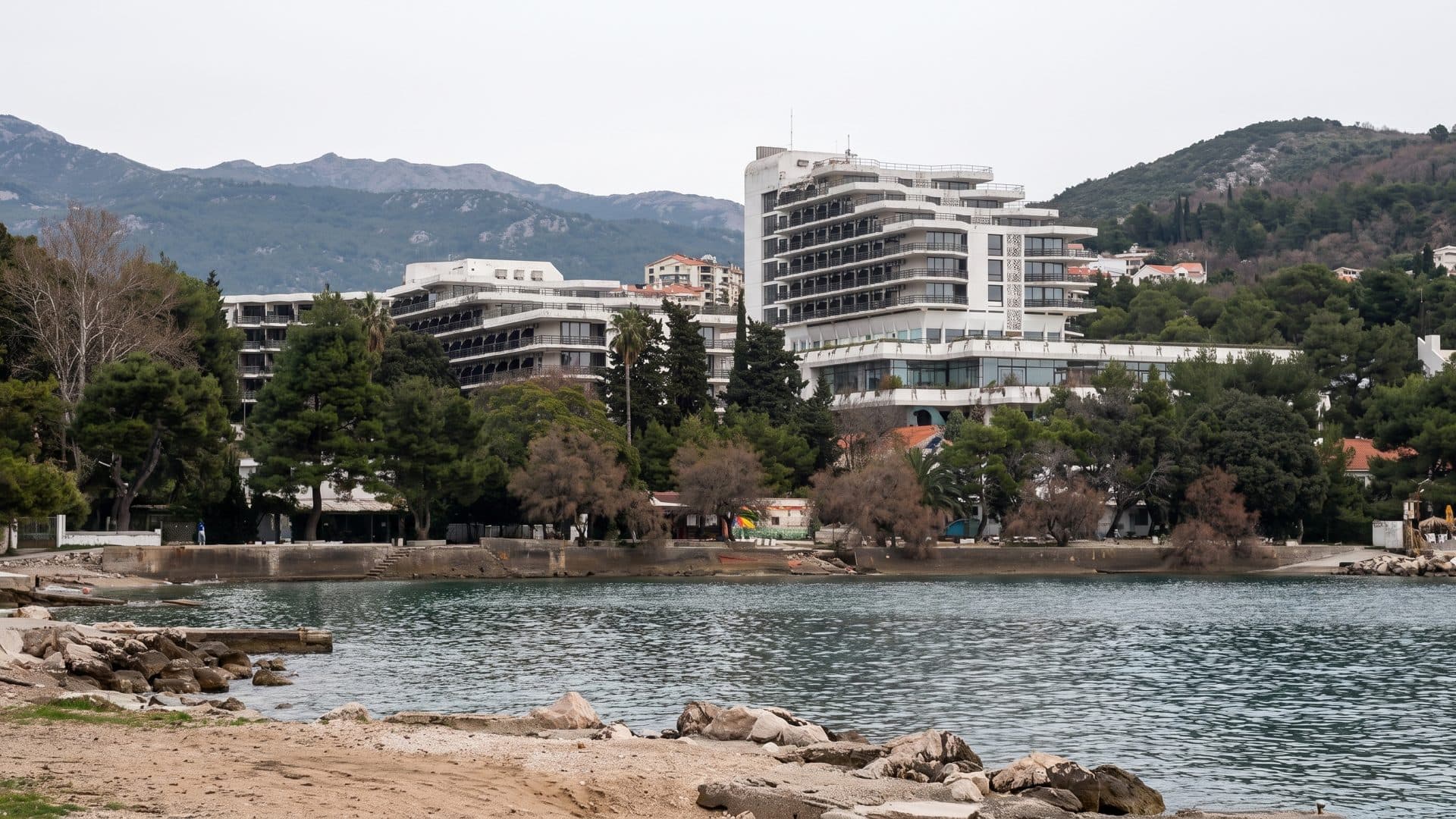 The terraced white blocks of the Igalo Institute seen across the bay, with the wooded hillside rising behind