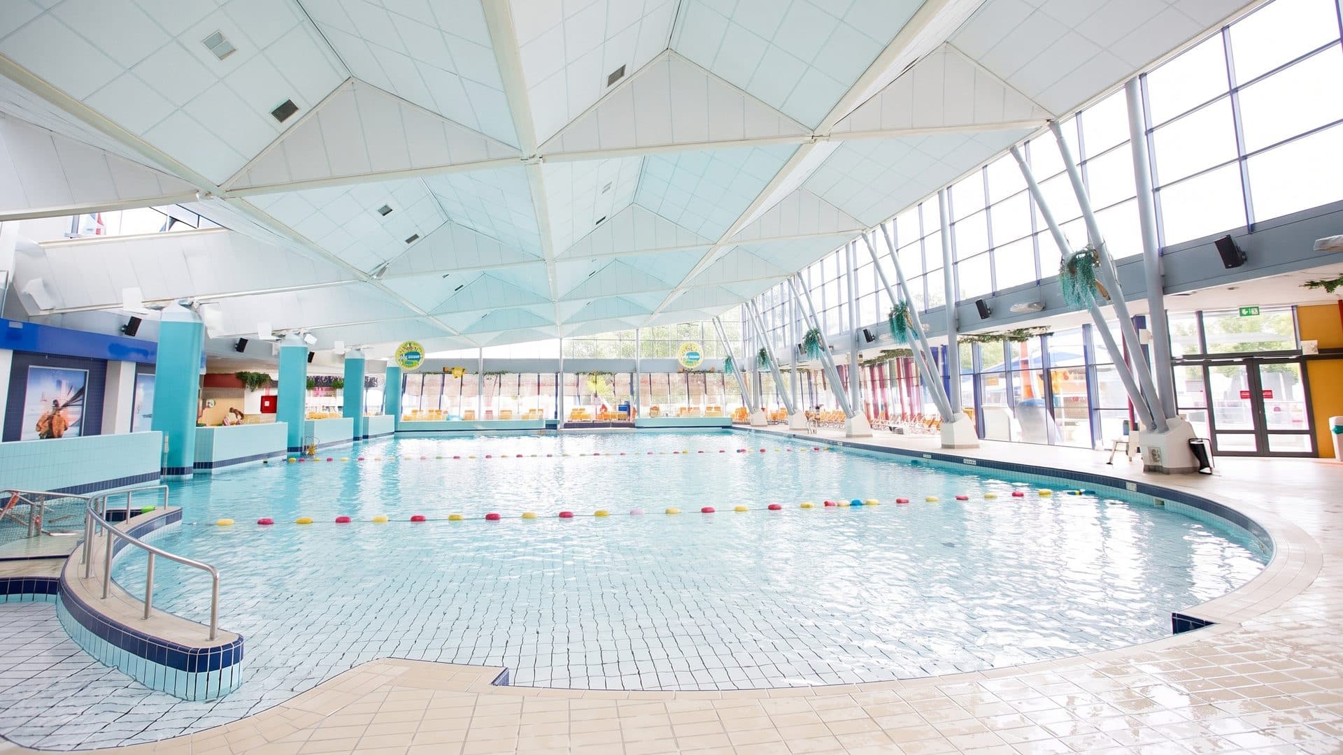 The curved leisure pool of the ir. Ottenbad with its tiled beach entry under the white tensile roof