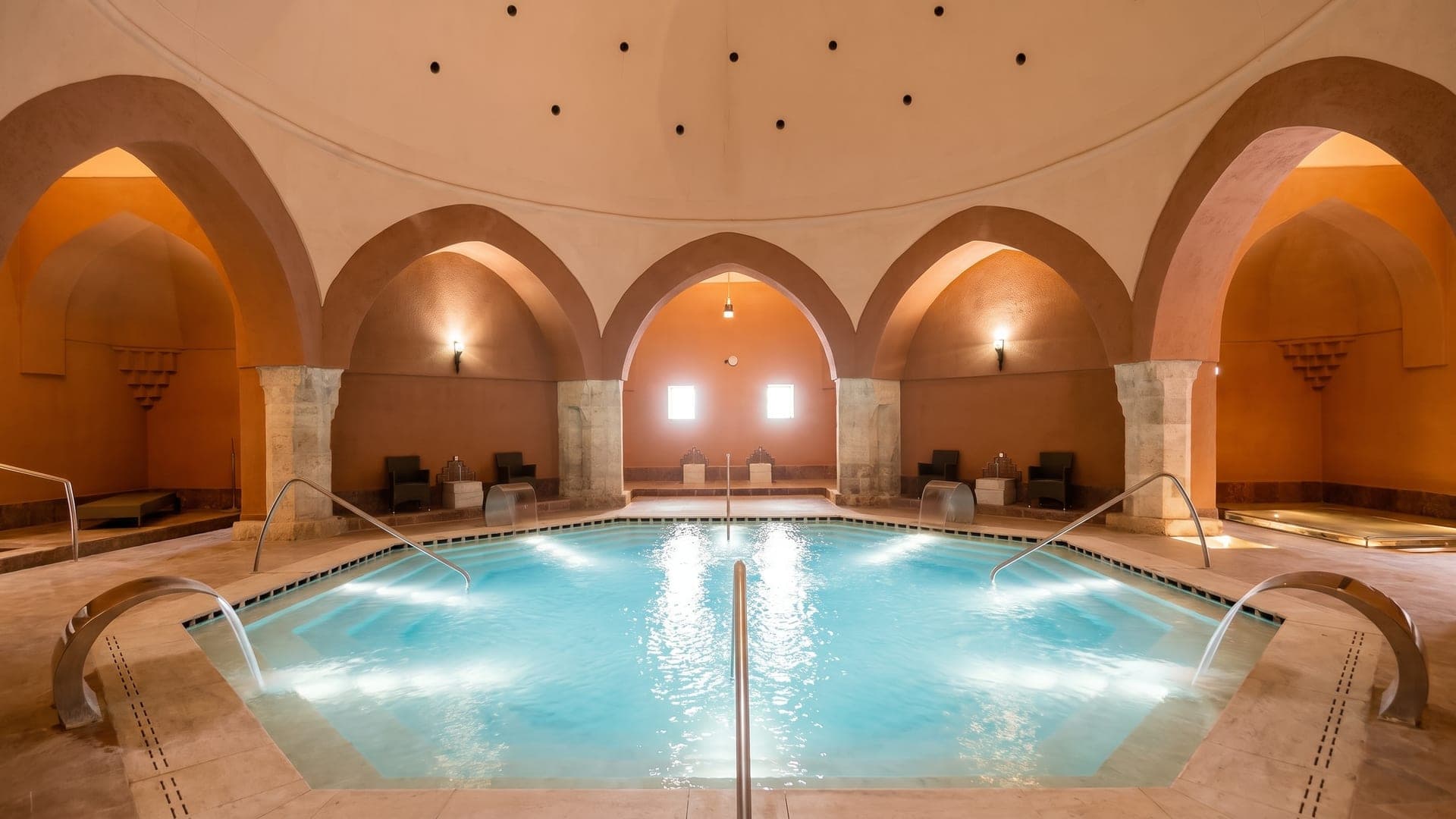 The octagonal pool of the Veli Bej bath in Budapest under its Ottoman dome, ringed by ochre arches and alcoves.