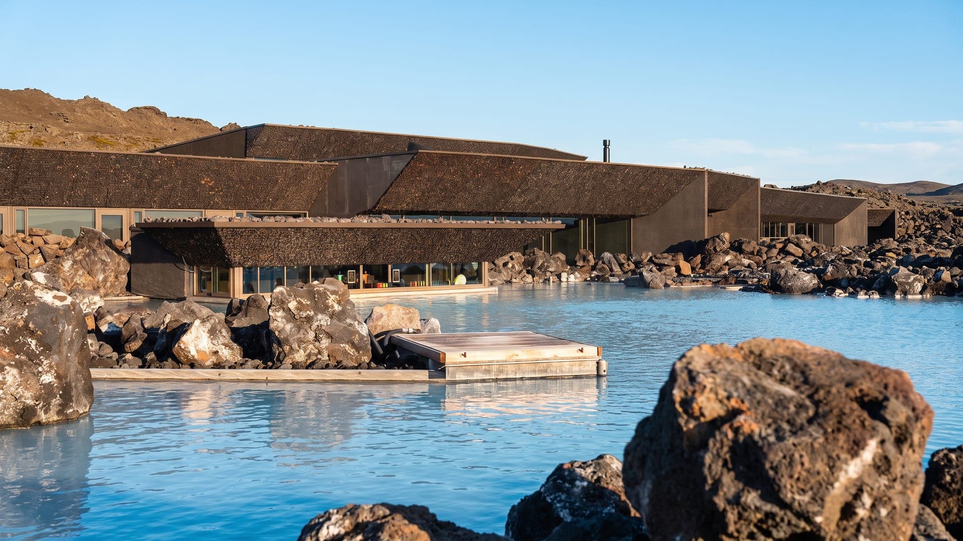 Milky blue lagoon among dark lava rocks, with a low turf-roofed building