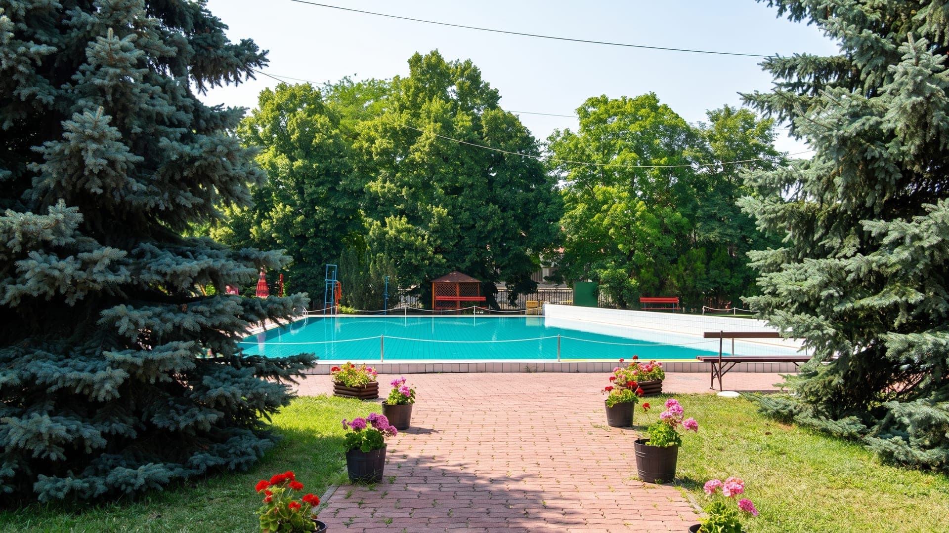 The outdoor pool at the thermal bath in Jaszbereny, among conifers with pots of flowers along the path.
