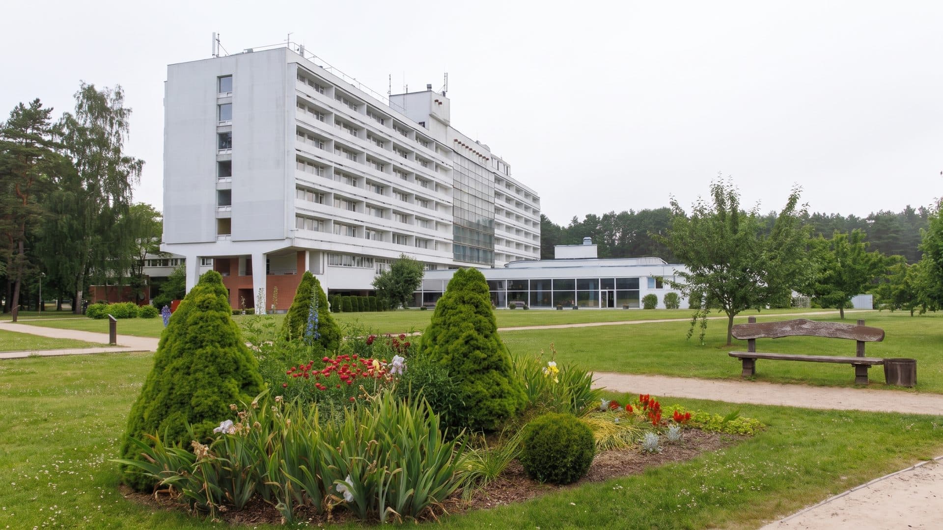 The long white sanatorium block at Jaunkemeri in Jurmala seen across its lawn, with conifers and flower beds in front