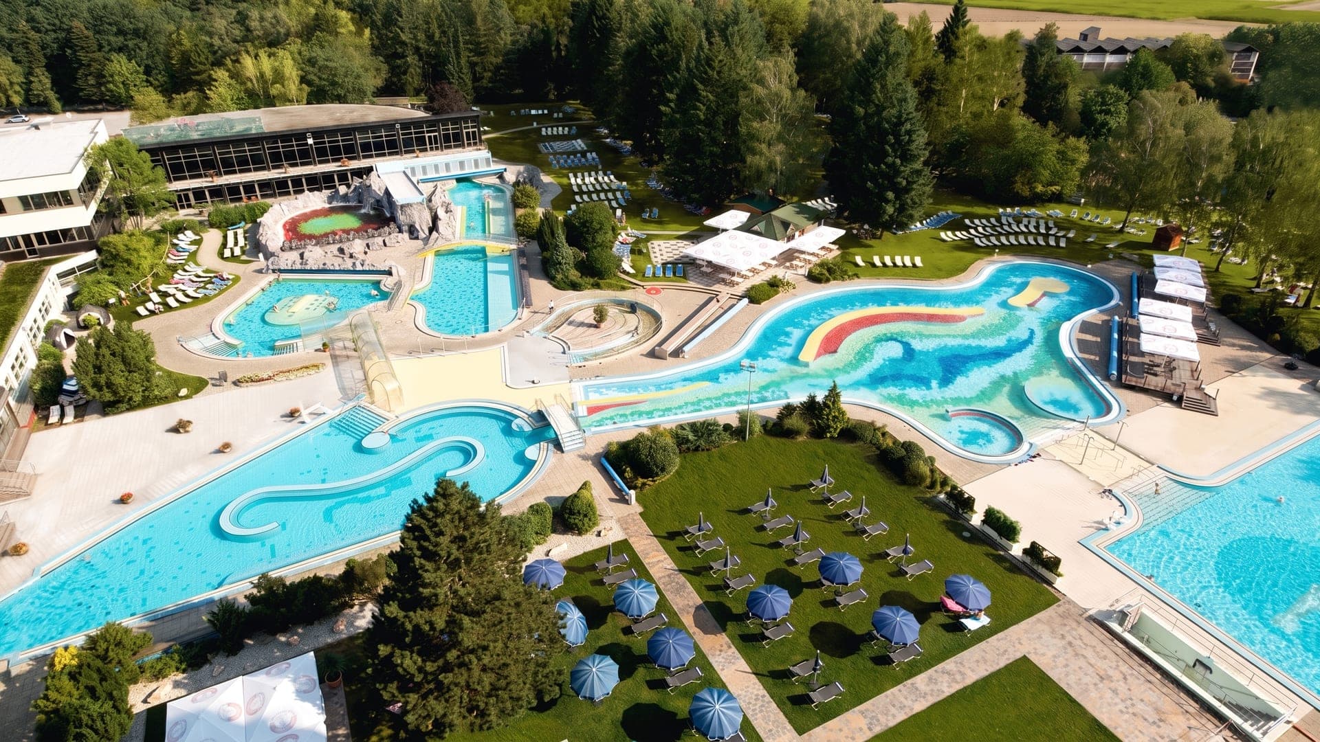 The Johannesbad Therme in Bad Fuessing seen from the air, its winding outdoor pools set among lawns and parasols.