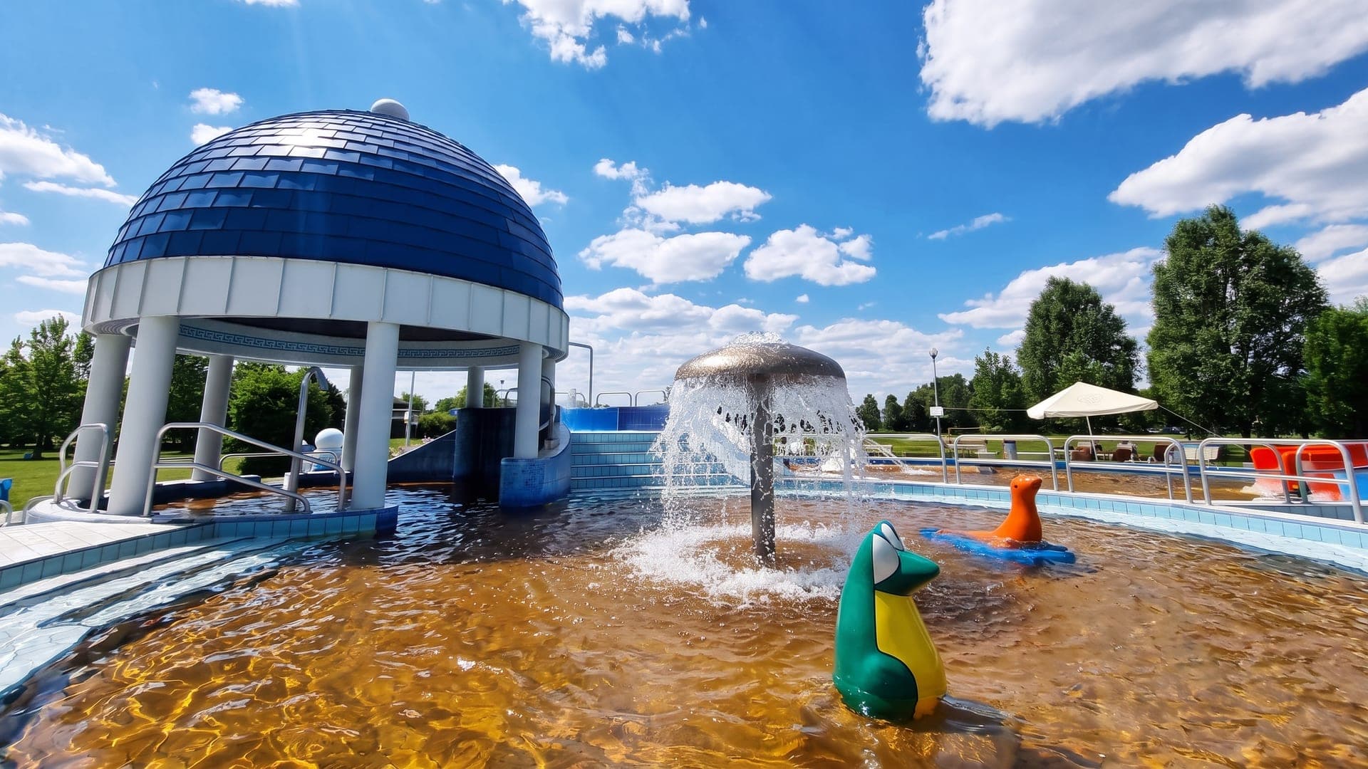 The blue-domed pavilion over the outdoor pool at Jonathermal in Kiskunmajsa, with a mushroom fountain in the thermal water.