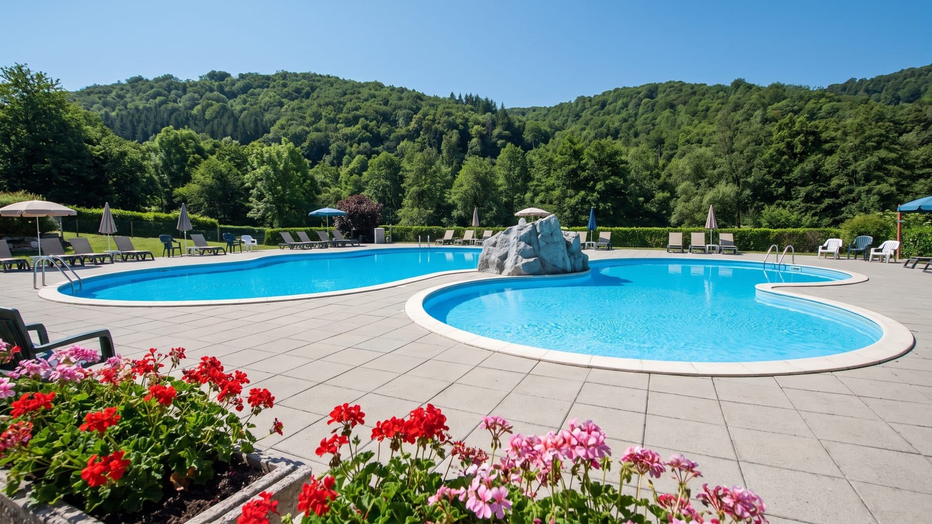The outdoor pools of the Karoli-Badepark with their rock feature below the wooded hills