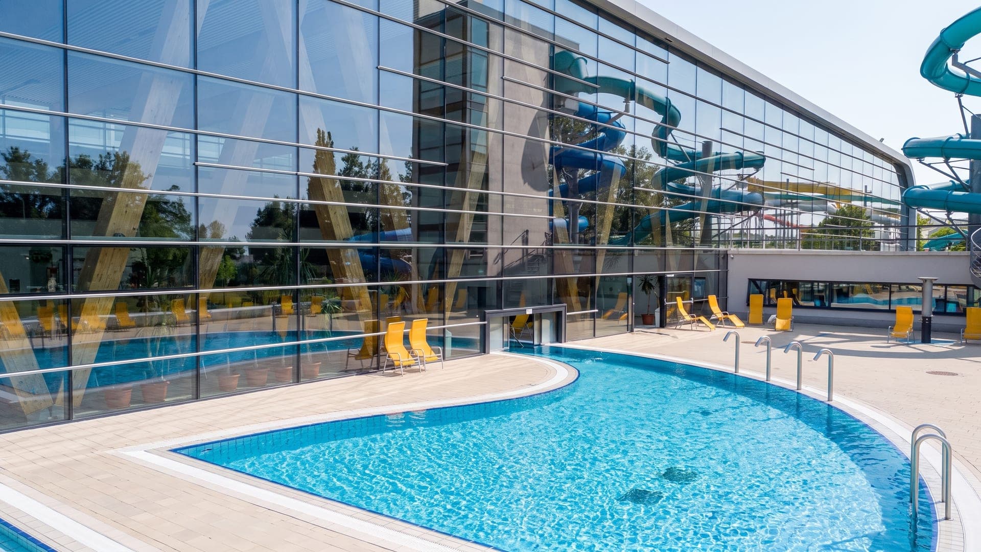 The outdoor pool at the Kecskemet bath, the waterslides reflected in the glass facade of the hall.