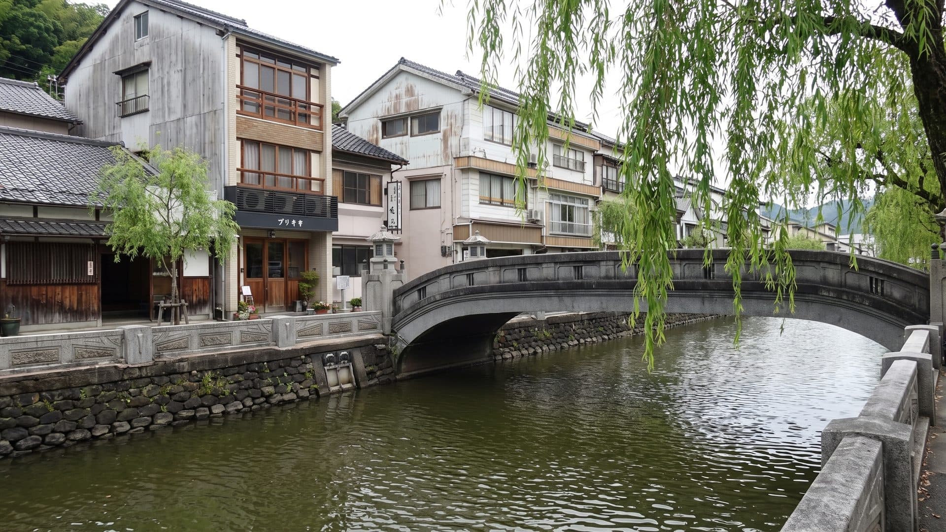 The canal at Kinosaki Onsen with its arched stone bridge and the wooden ryokan fronts lining the water under willows